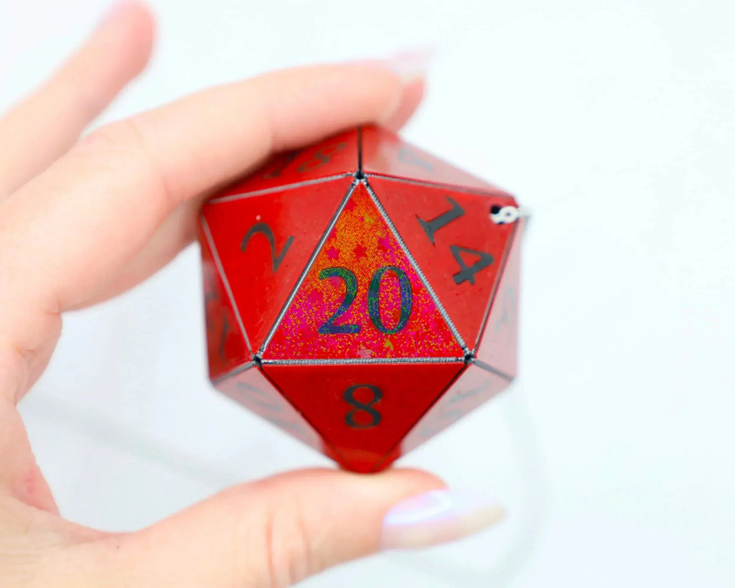 Hand holding a large red holographic 20-sided dice charm with black numbers, RPG accessory