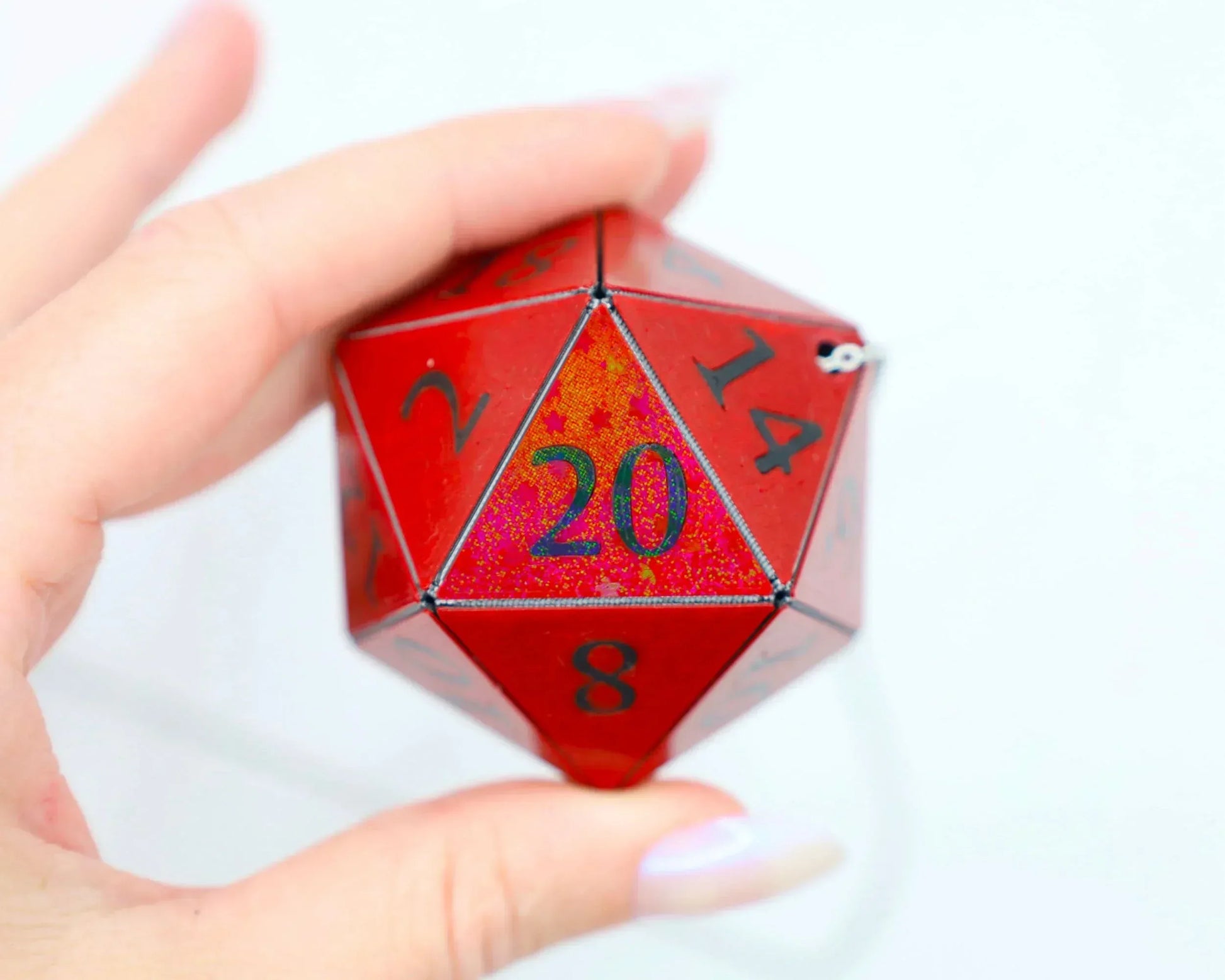 Hand holding a large red holographic 20-sided dice charm with black numbers, RPG accessory