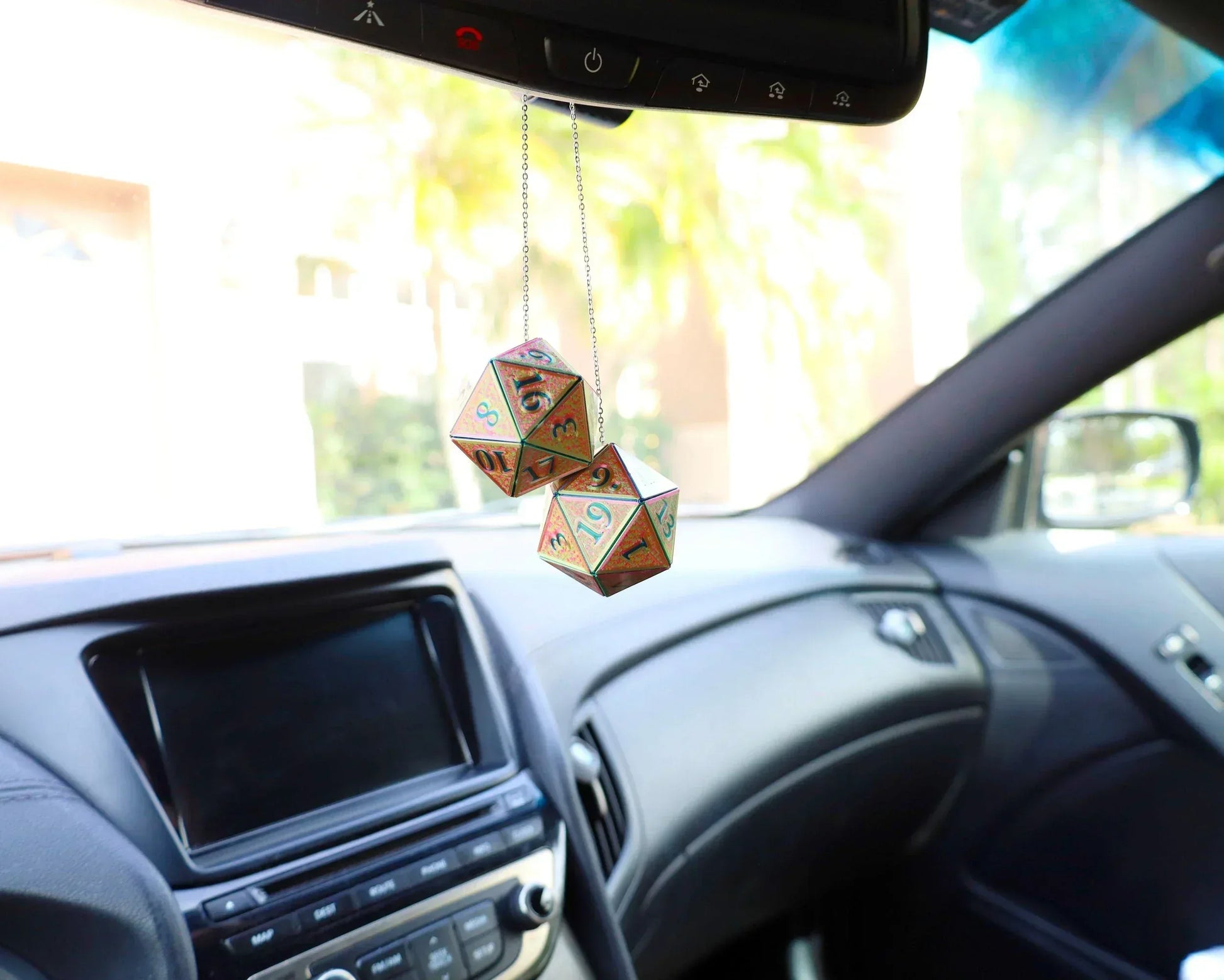 Holographic twenty-sided dice car charm hanging from rearview mirror in a vehicle interior