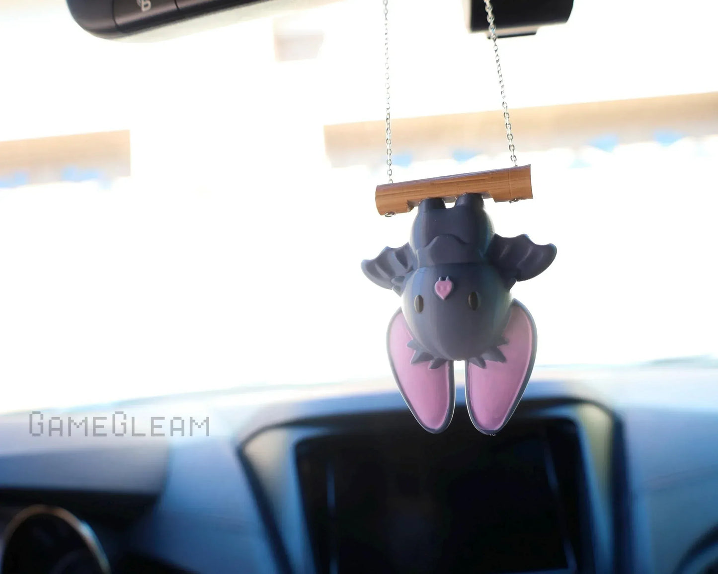 Cute handmade bat car charm with pink ears hanging from a chain in a car interior.