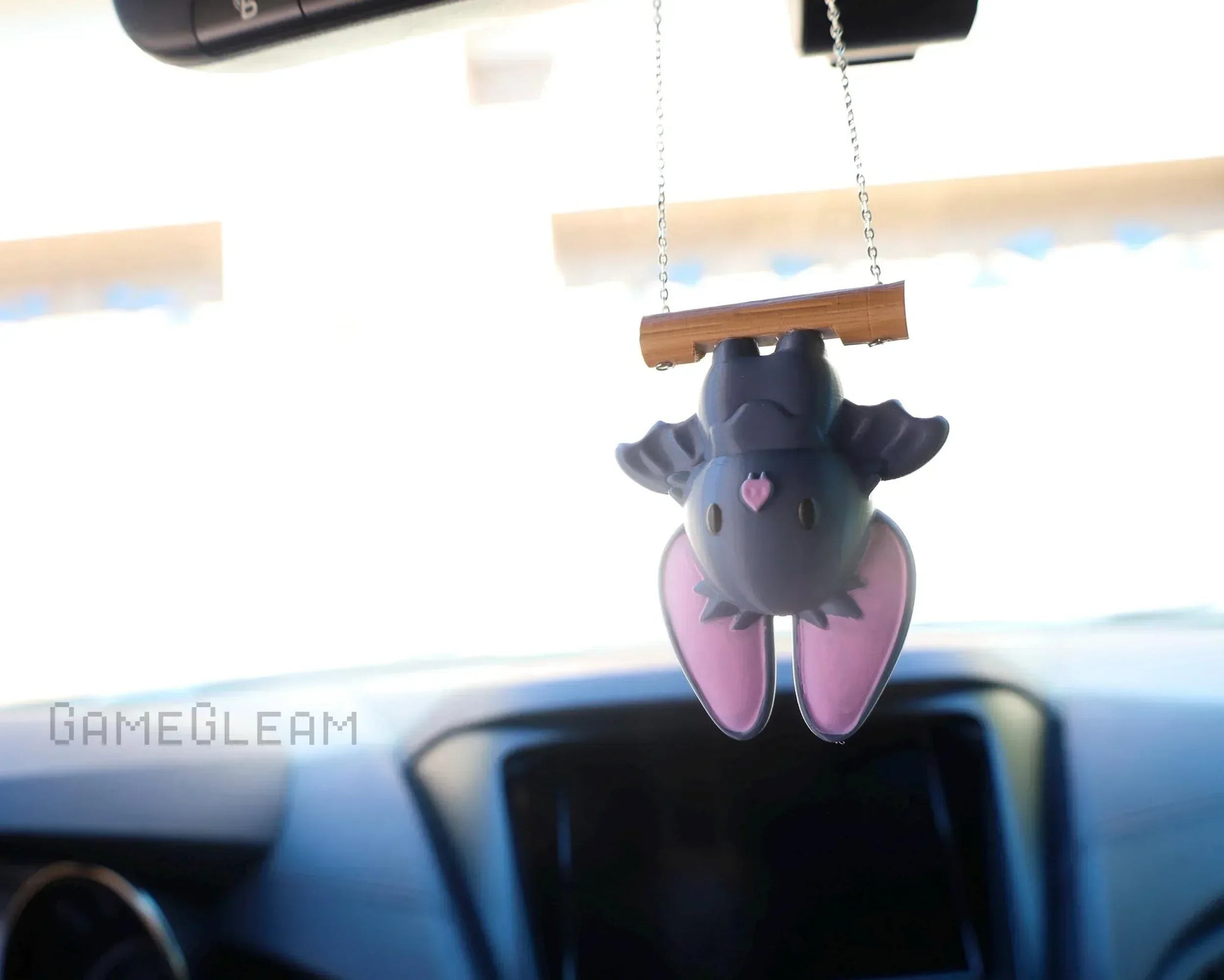 Cute handmade bat car charm with pink ears hanging from a chain in a car interior.