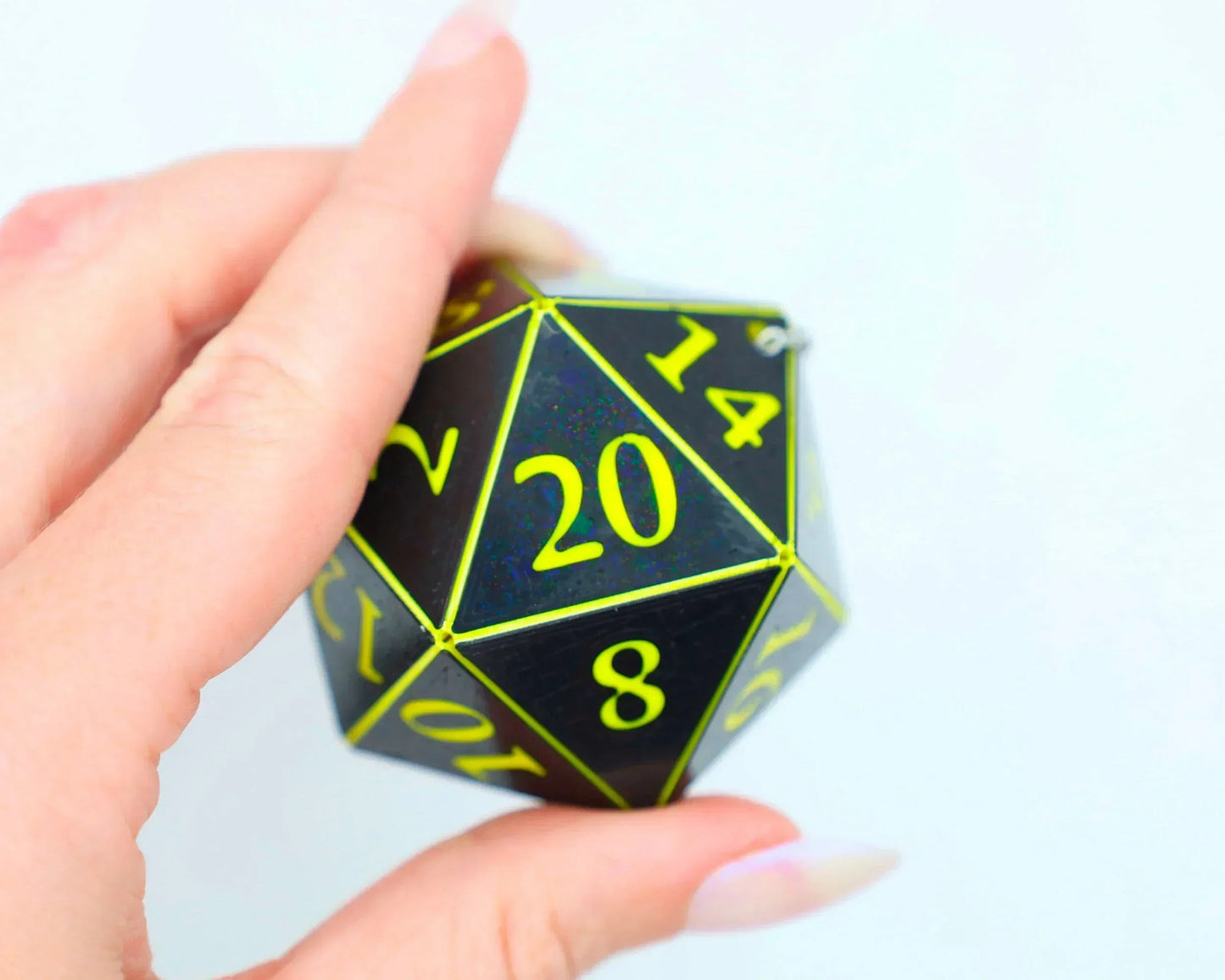 Hand holding a holographic black twenty-sided dice charm with neon yellow numbers