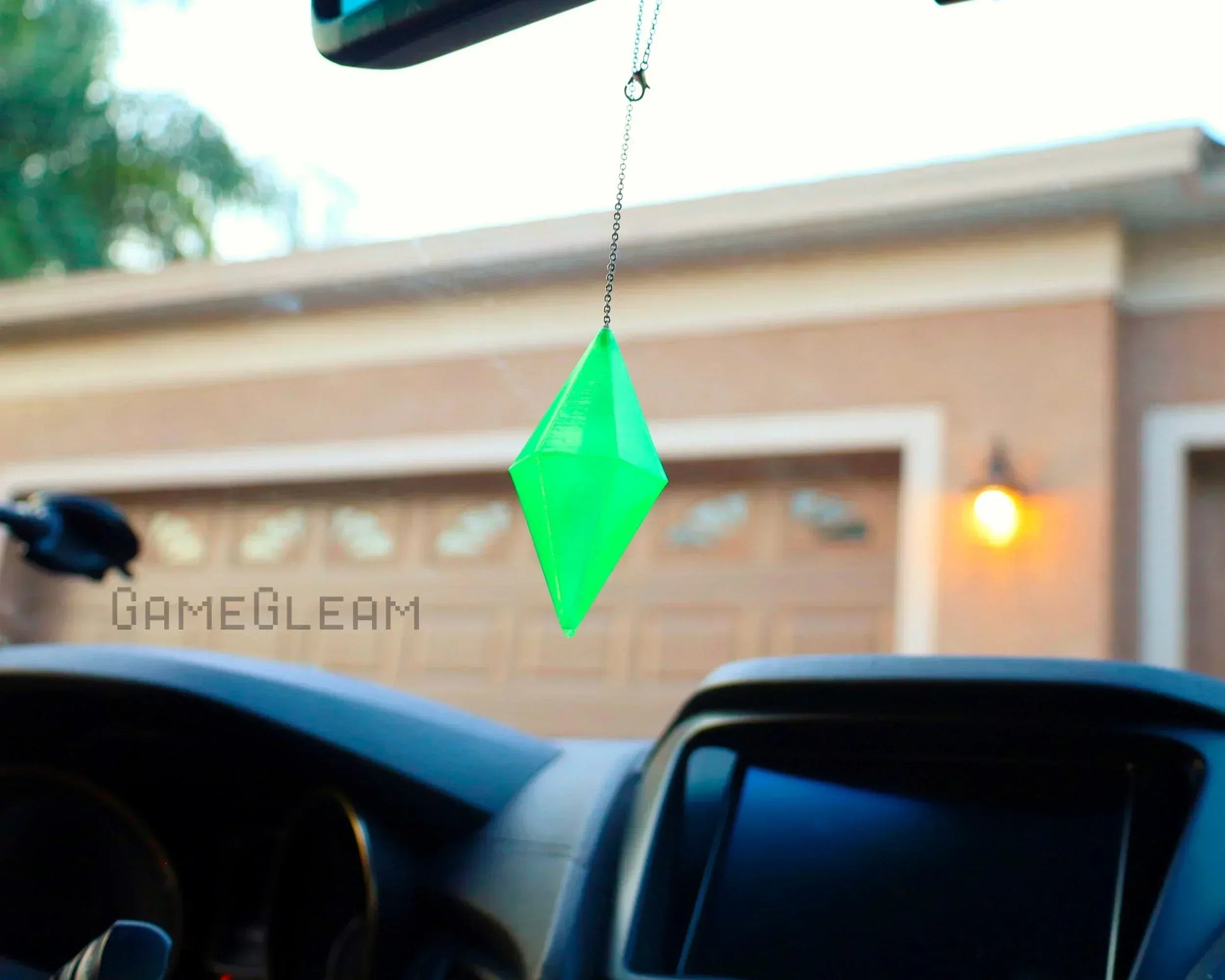 Green crystal-shaped car charm hanging from rearview mirror, photographed in a car interior
