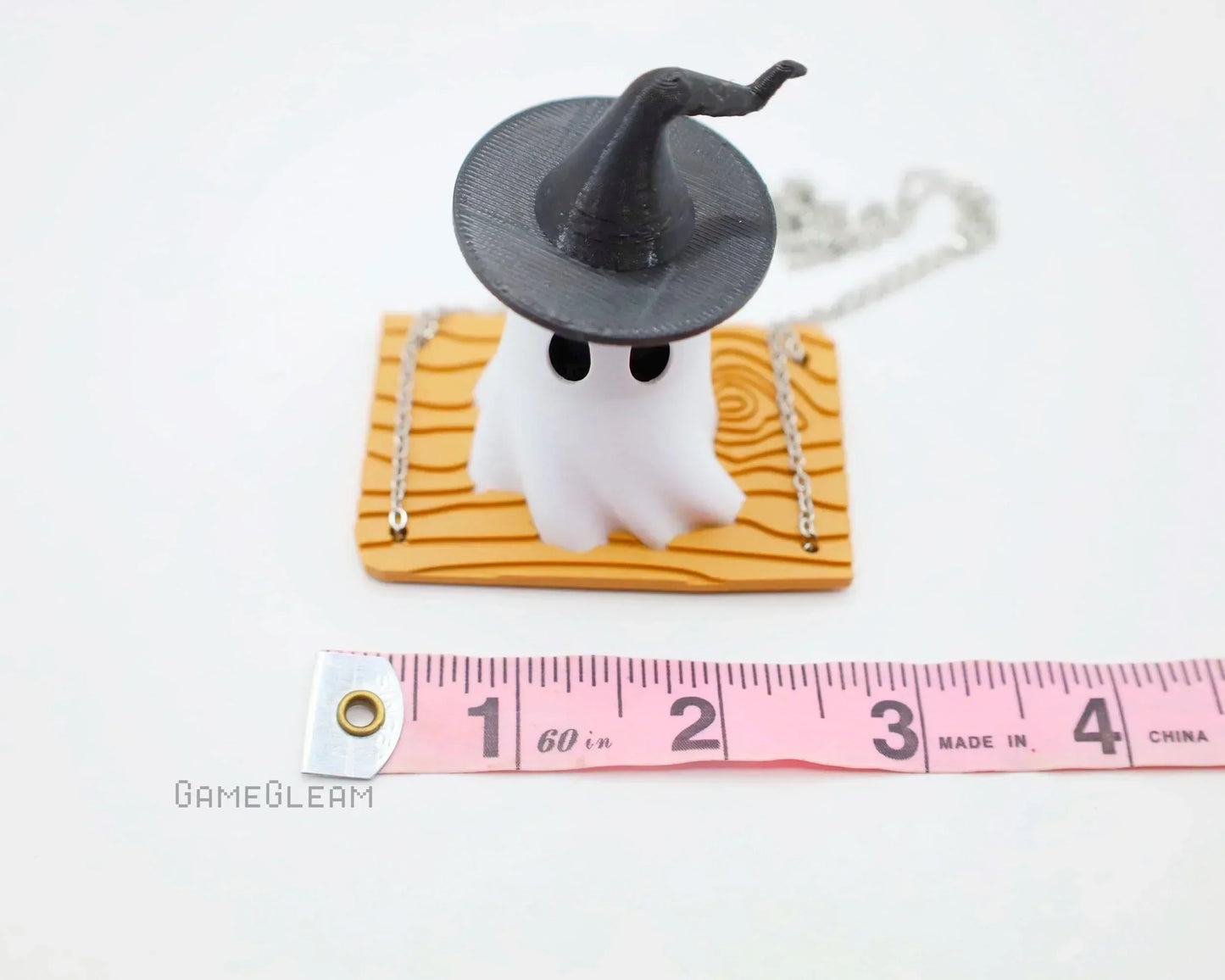 Handmade ghost charm with witch hat on wood base, chain accessory, next to measuring tape