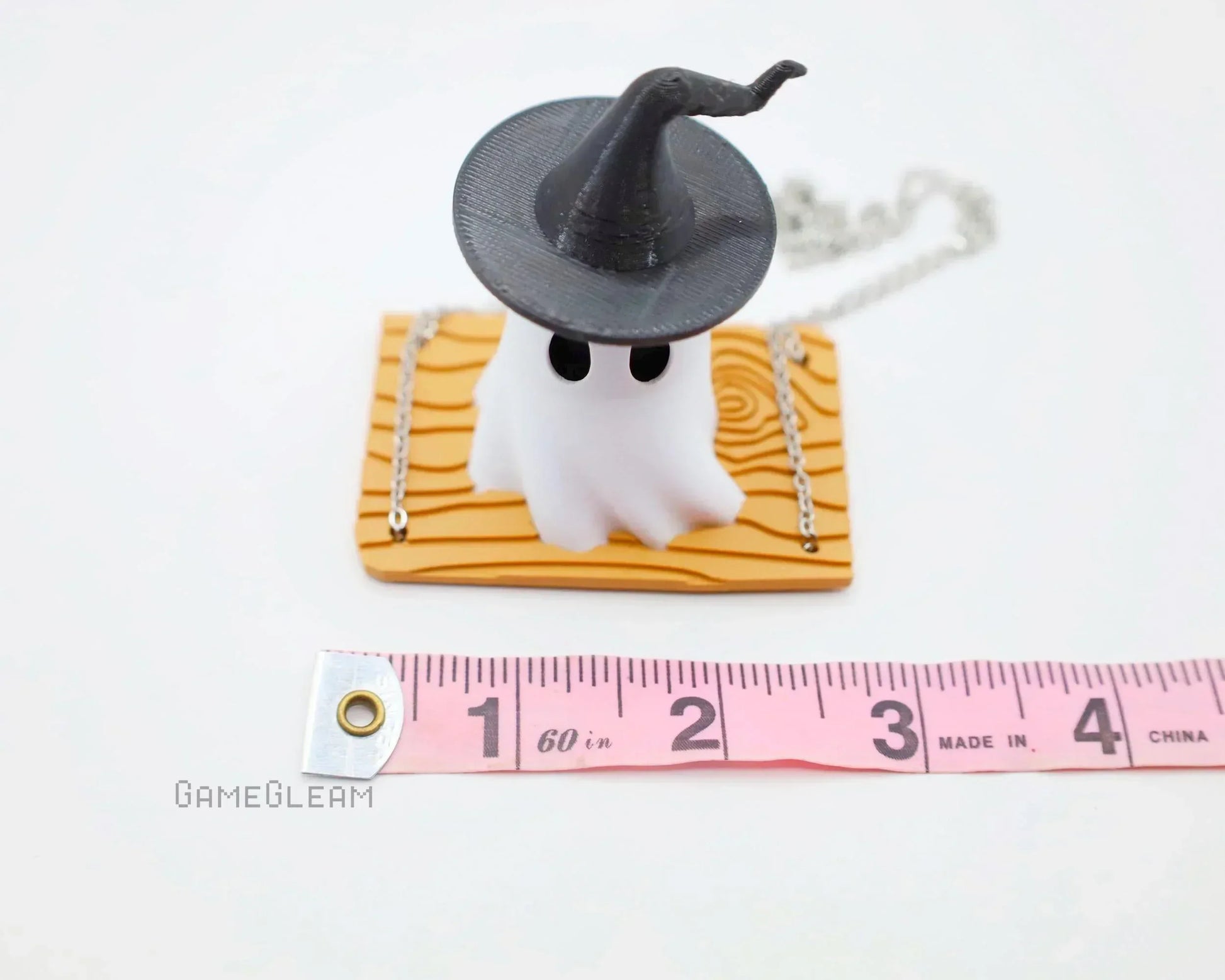 Handmade ghost charm with witch hat on wood base, chain accessory, next to measuring tape