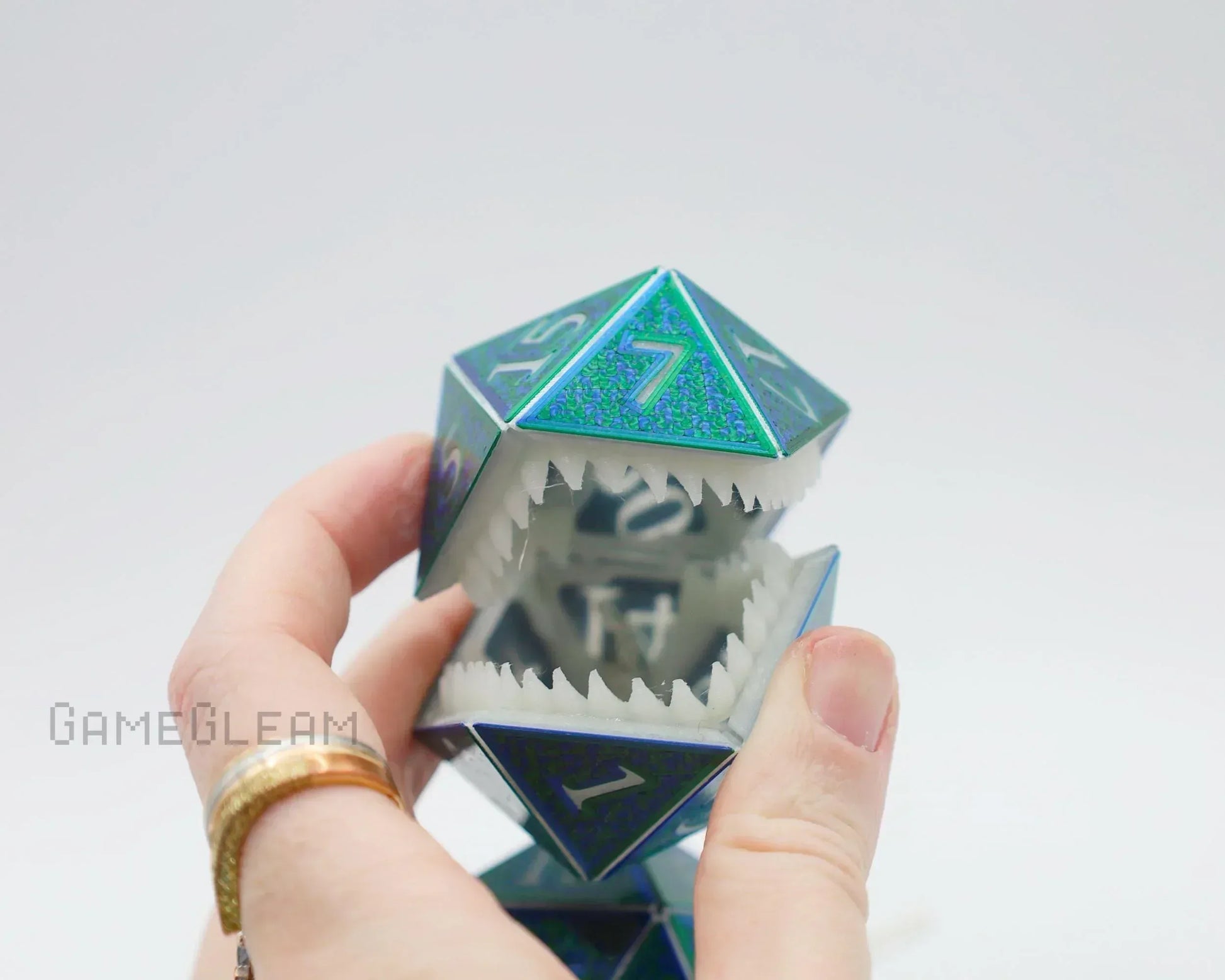 Hand holding a holographic blue polyhedral dice charm with sharp monster teeth detail