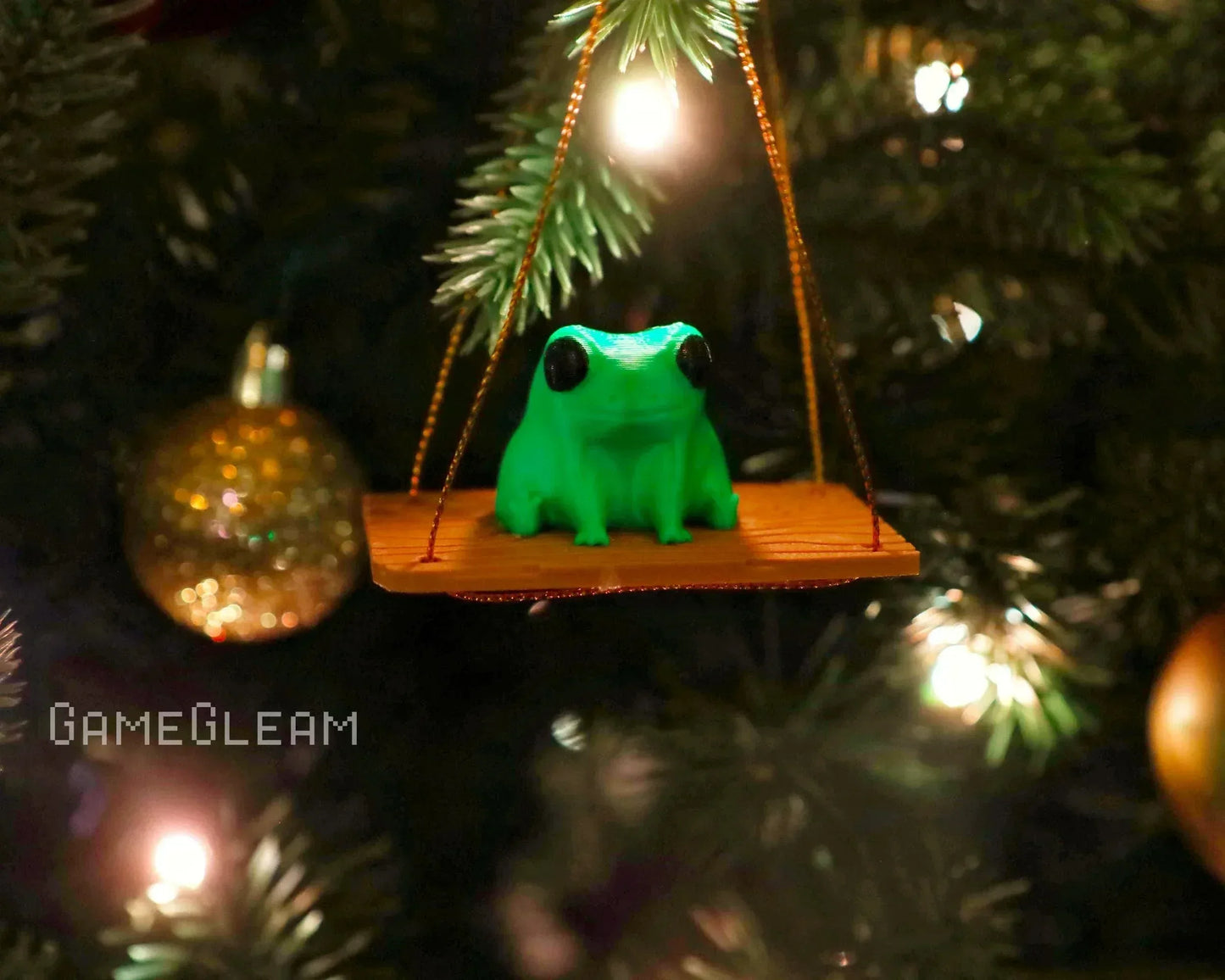 Green frog ornament sitting on a swing, hanging on a decorated Christmas tree.