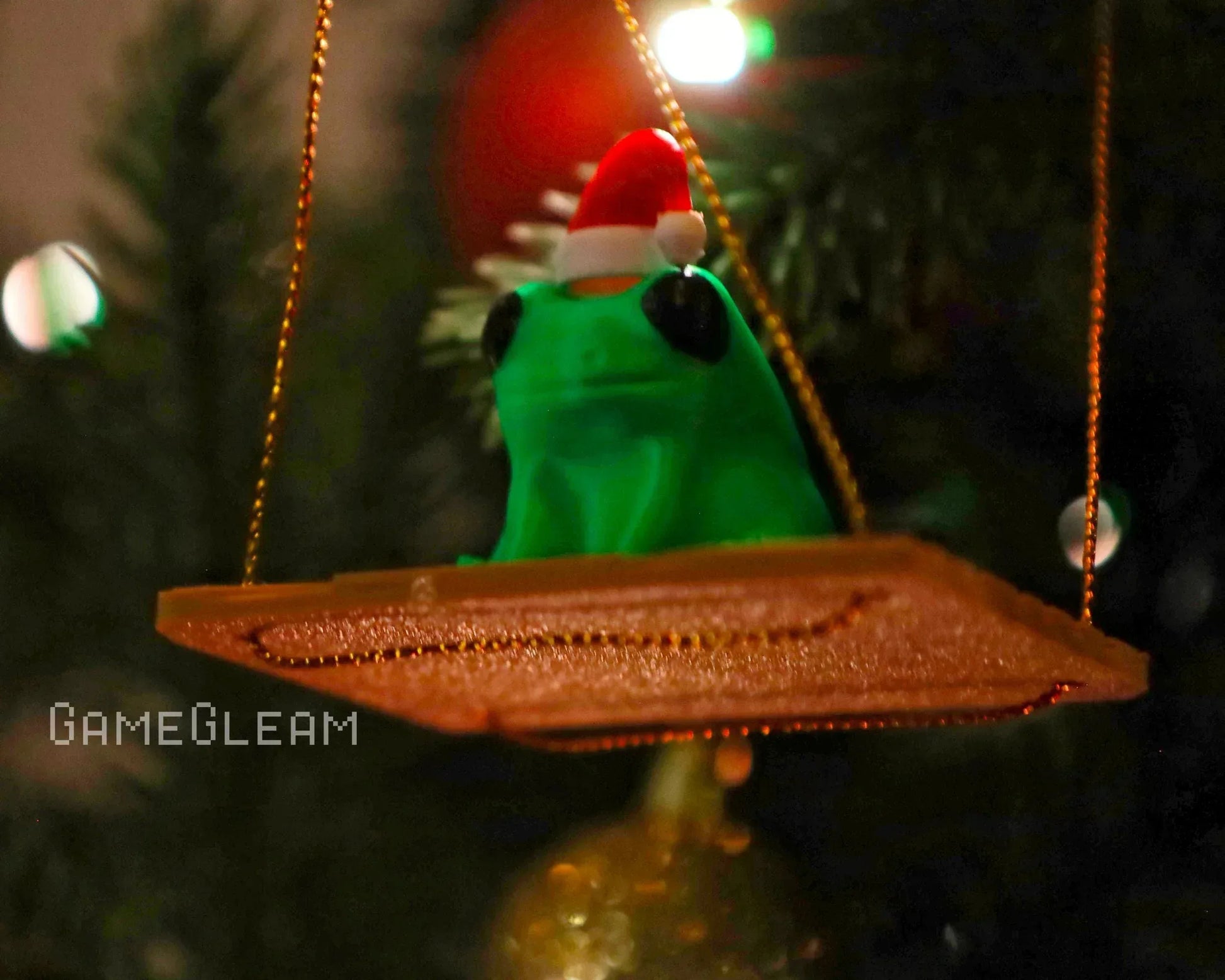Green frog figurine wearing a Santa hat sitting on a gold platform, Christmas ornament