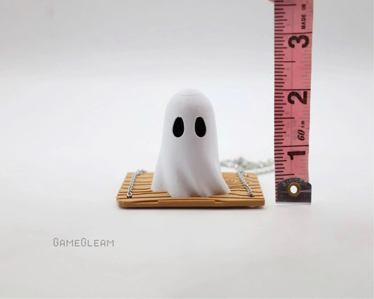 Miniature white ghost figurine with black eyes on a wooden base, measured with a ruler