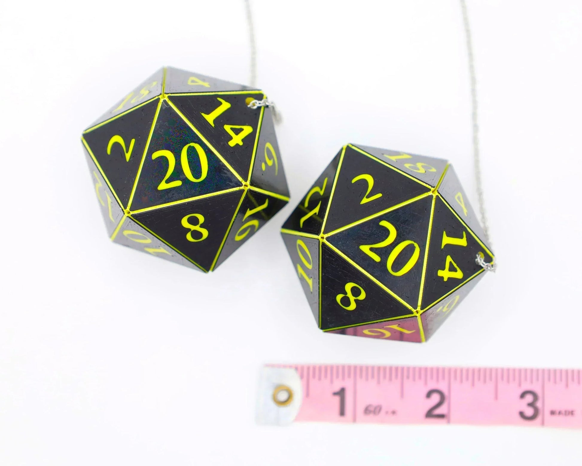 Pair of large black twenty-sided dice with yellow numbers on a chain, beside a tape measure