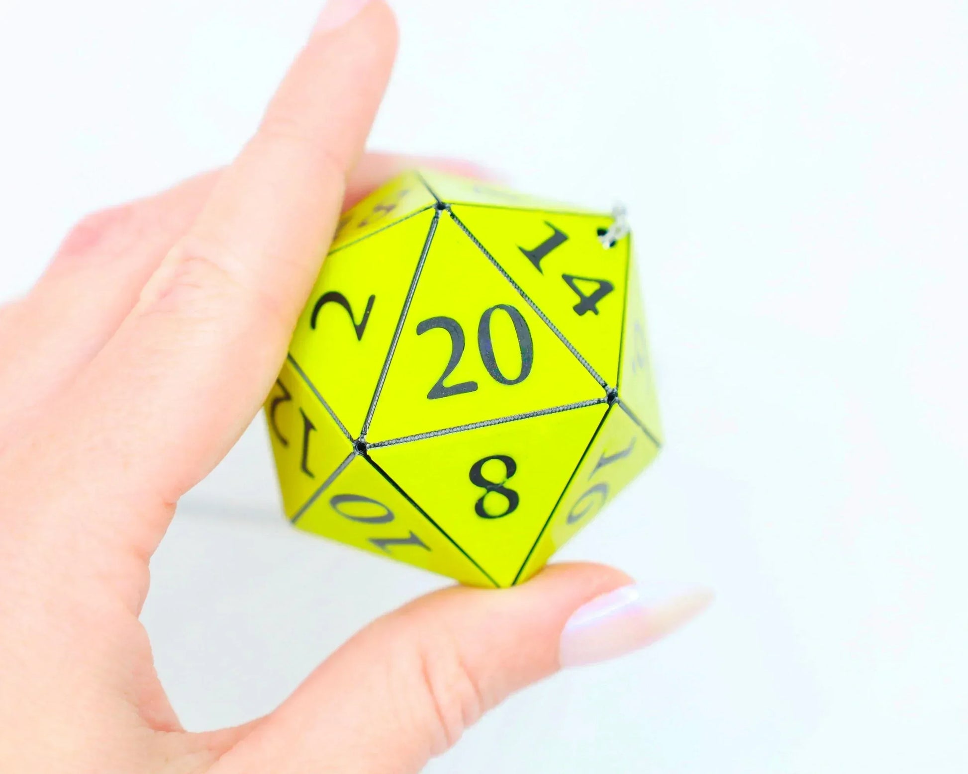 Hand holding a neon yellow 20-sided dice charm for tabletop RPG gaming fans