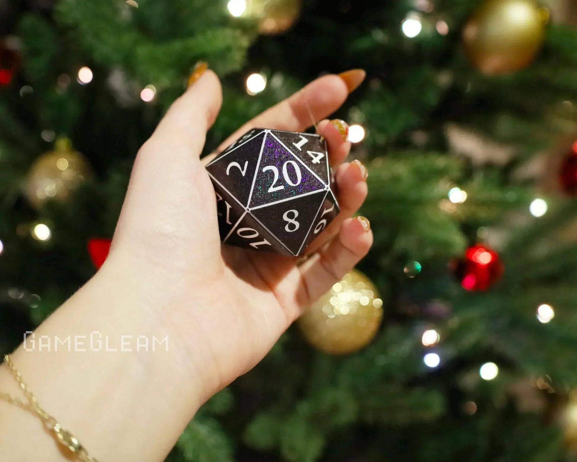 Hand holding a holographic black 20-sided dice ornament in front of a decorated Christmas tree