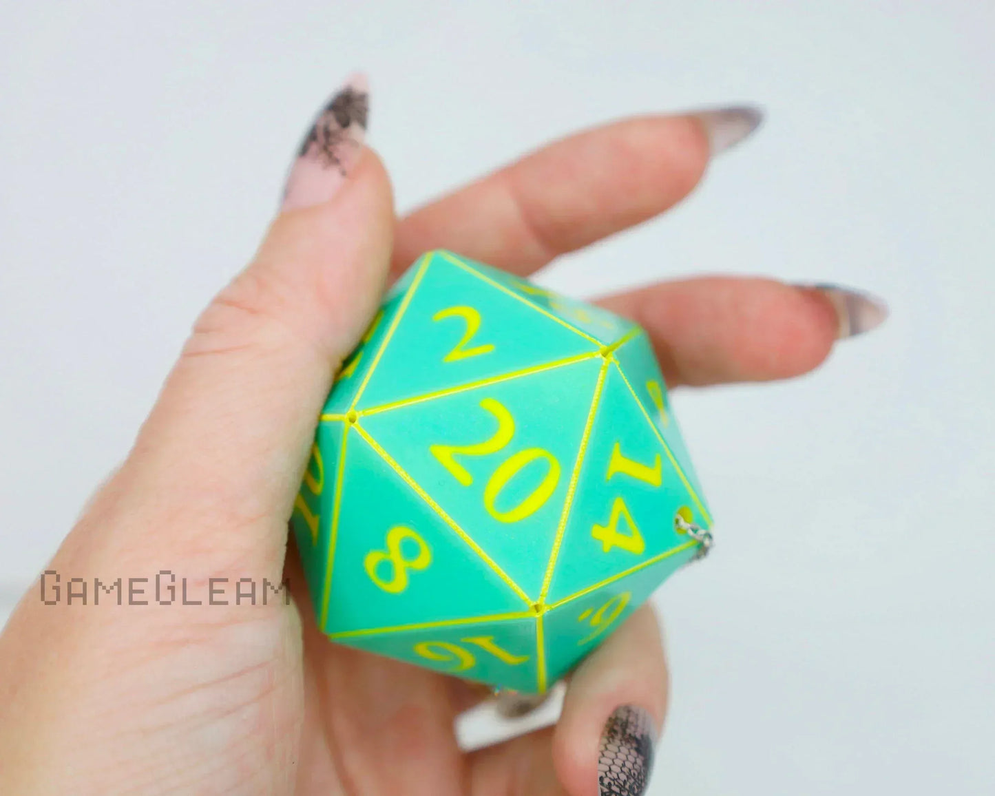 Hand holding large teal twenty-sided dice with yellow numbers, keychain style accessory