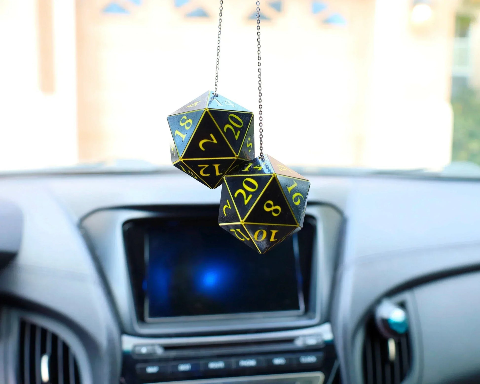 Black and yellow twenty-sided dice car charm hanging from rearview mirror in a modern car.