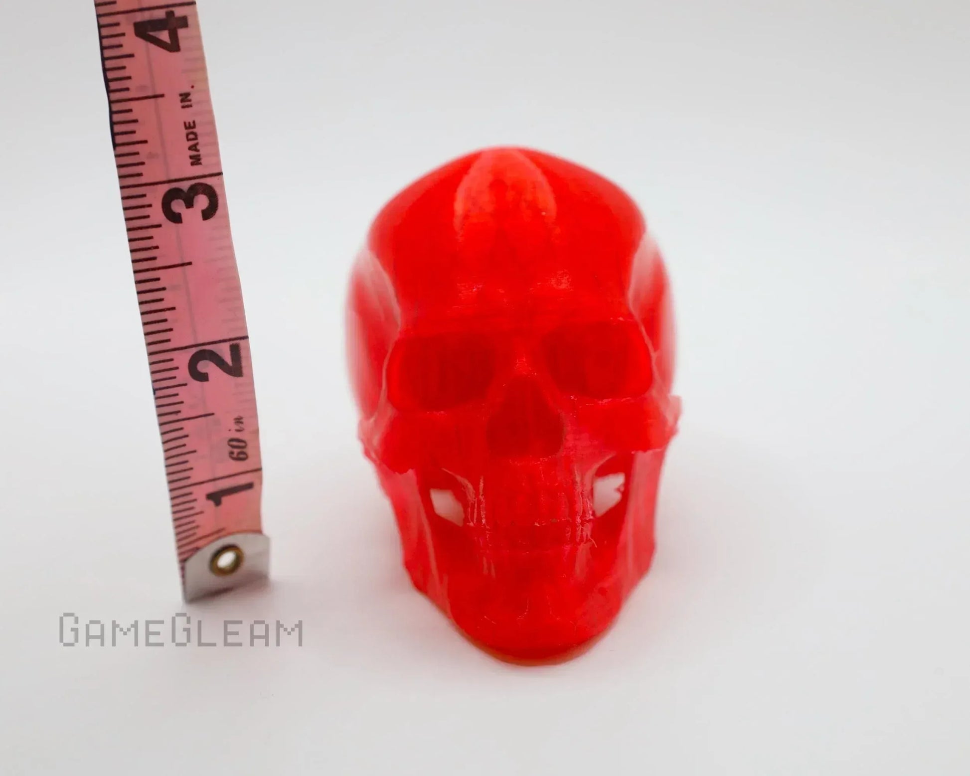 Bright red resin skull figurine next to measuring tape on white background