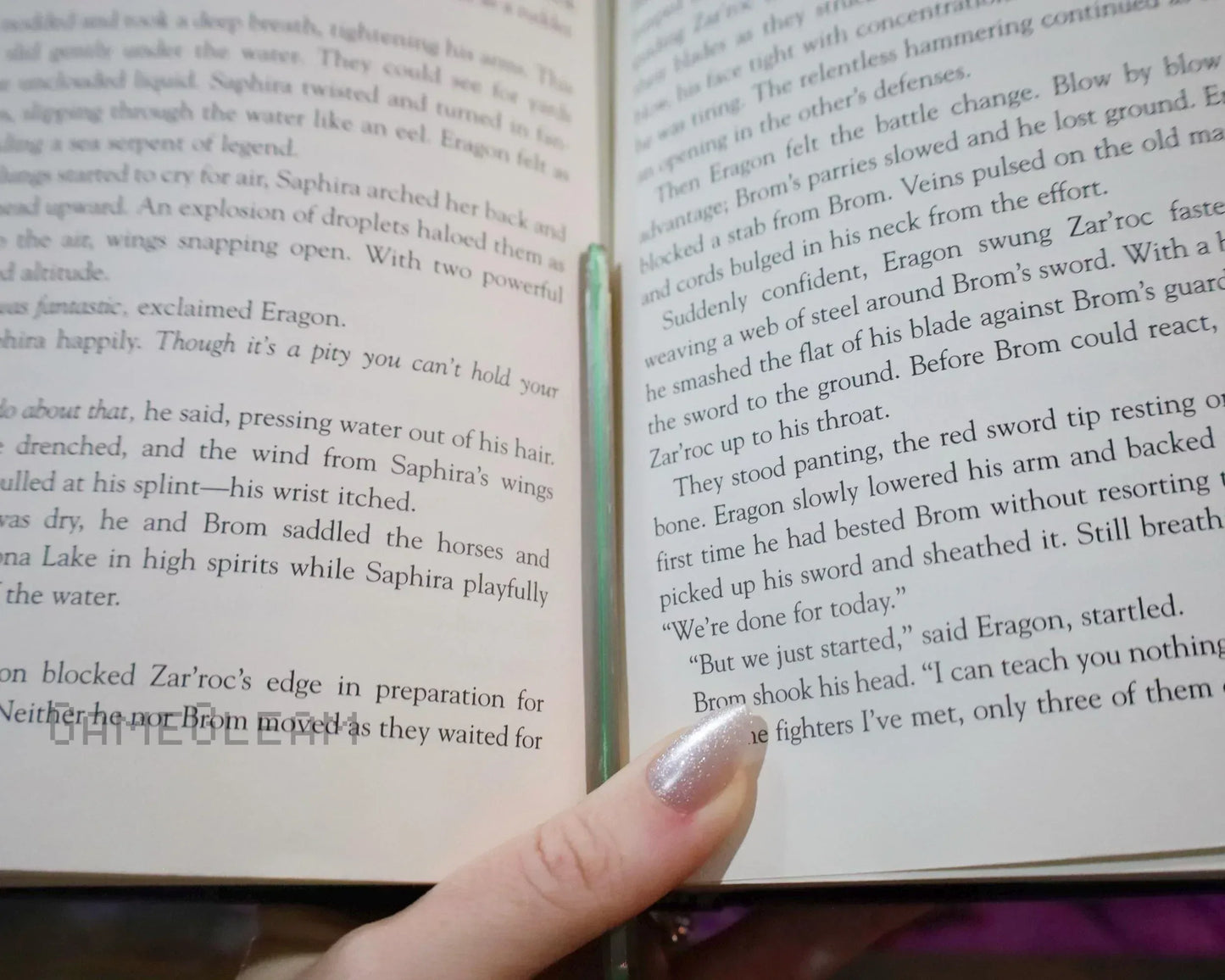 Hand holding open fantasy novel with shiny silver nail polish and text visible
