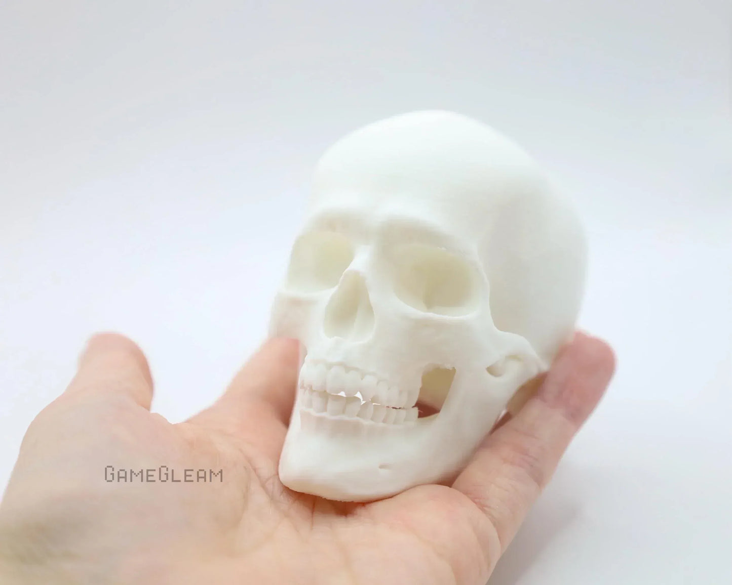 Hand holding a small white 3D printed human skull figurine on a plain background