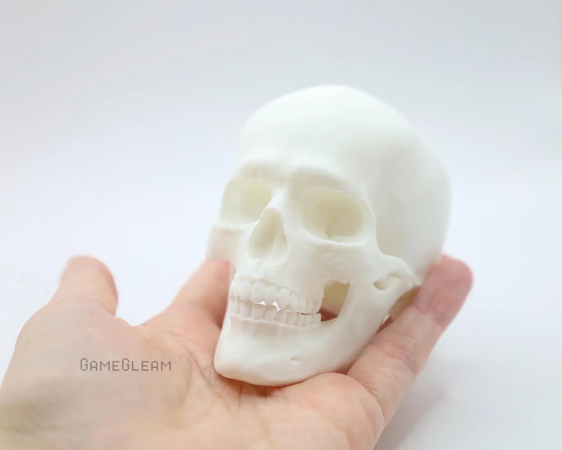 Hand holding a small white 3D printed human skull figurine on a plain background