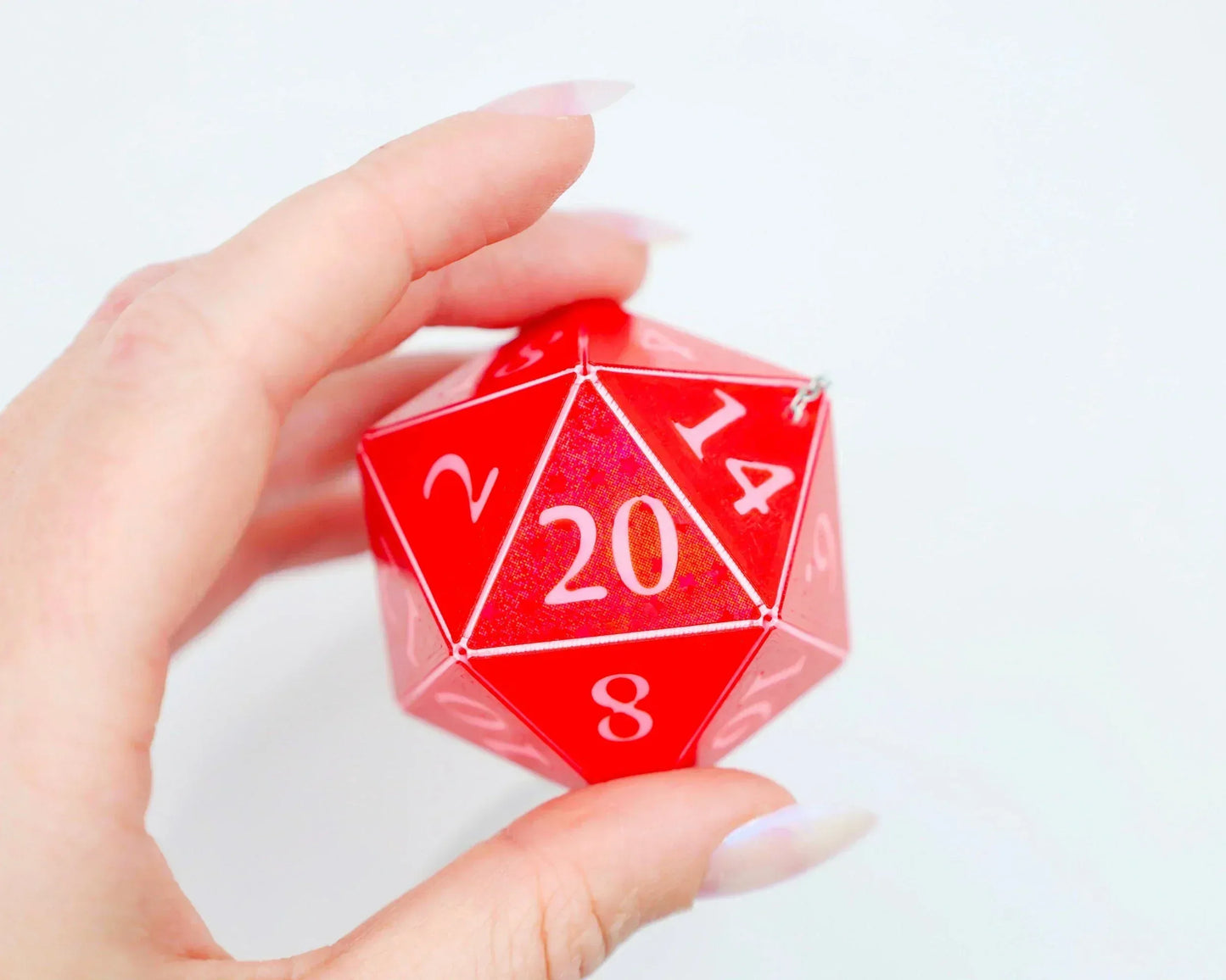 Hand holding a red 20-sided dice charm with white numbers on a white background