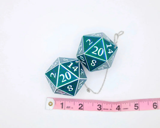 Pair of teal holographic 20-sided dice on a chain, shown with a pink measuring tape