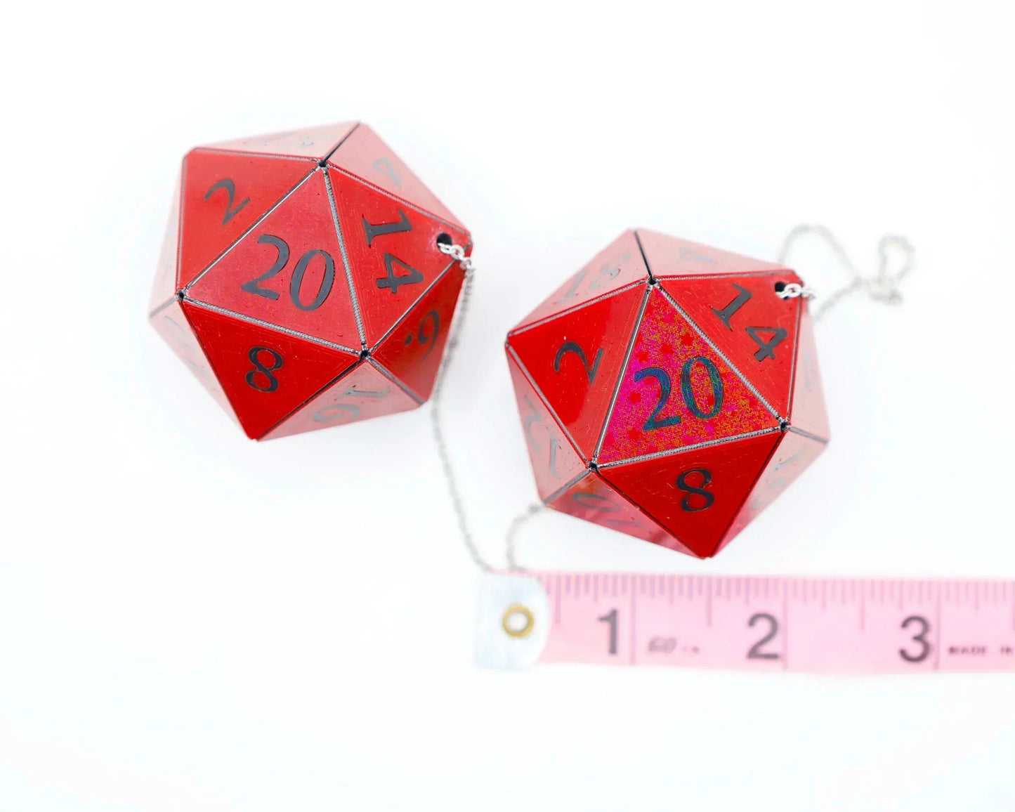 Pair of red 20-sided dice charms with chain, shown next to a measuring tape for scale.