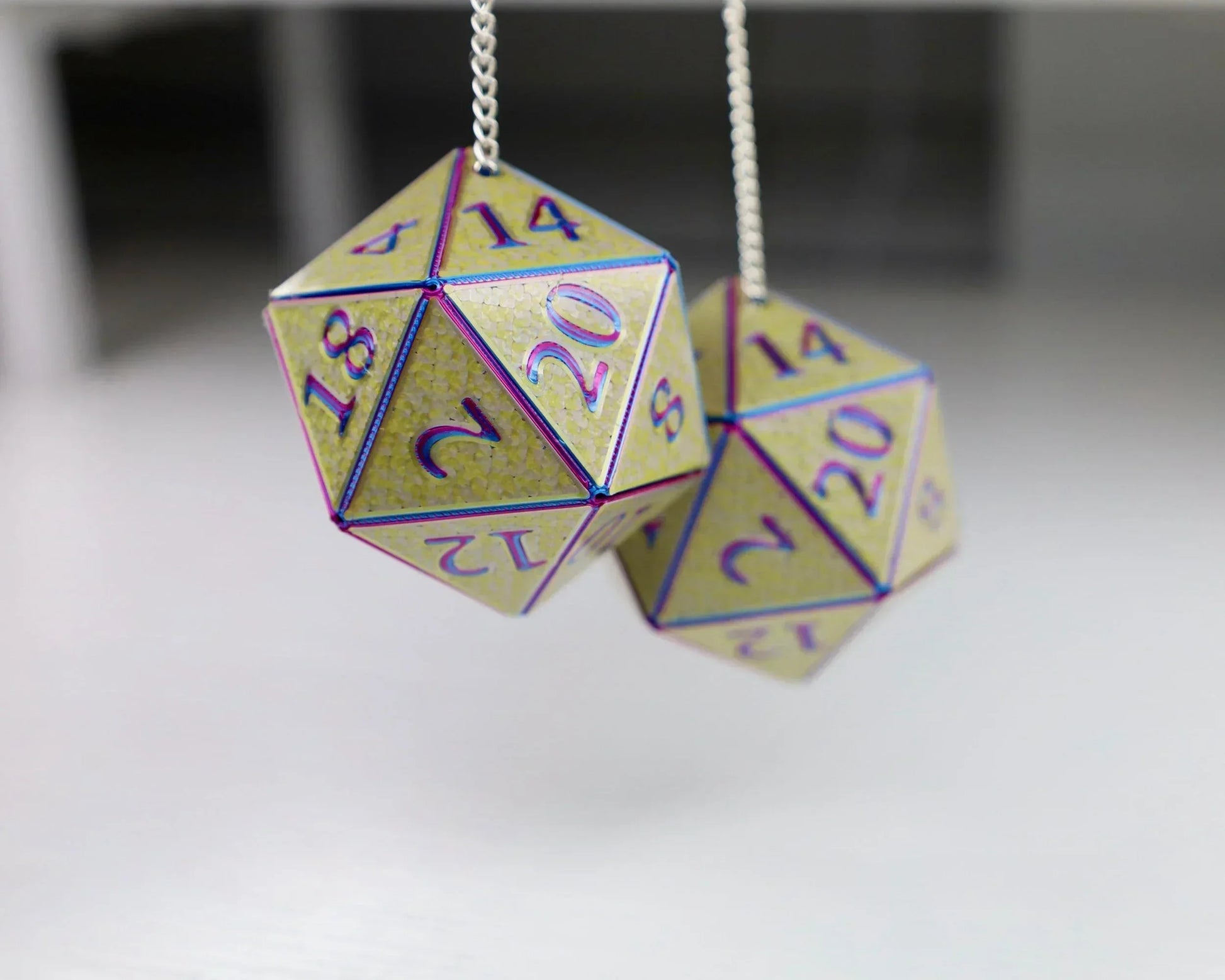 Pair of holographic yellow 20-sided dice hanging from a silver chain, tabletop gaming accessory.