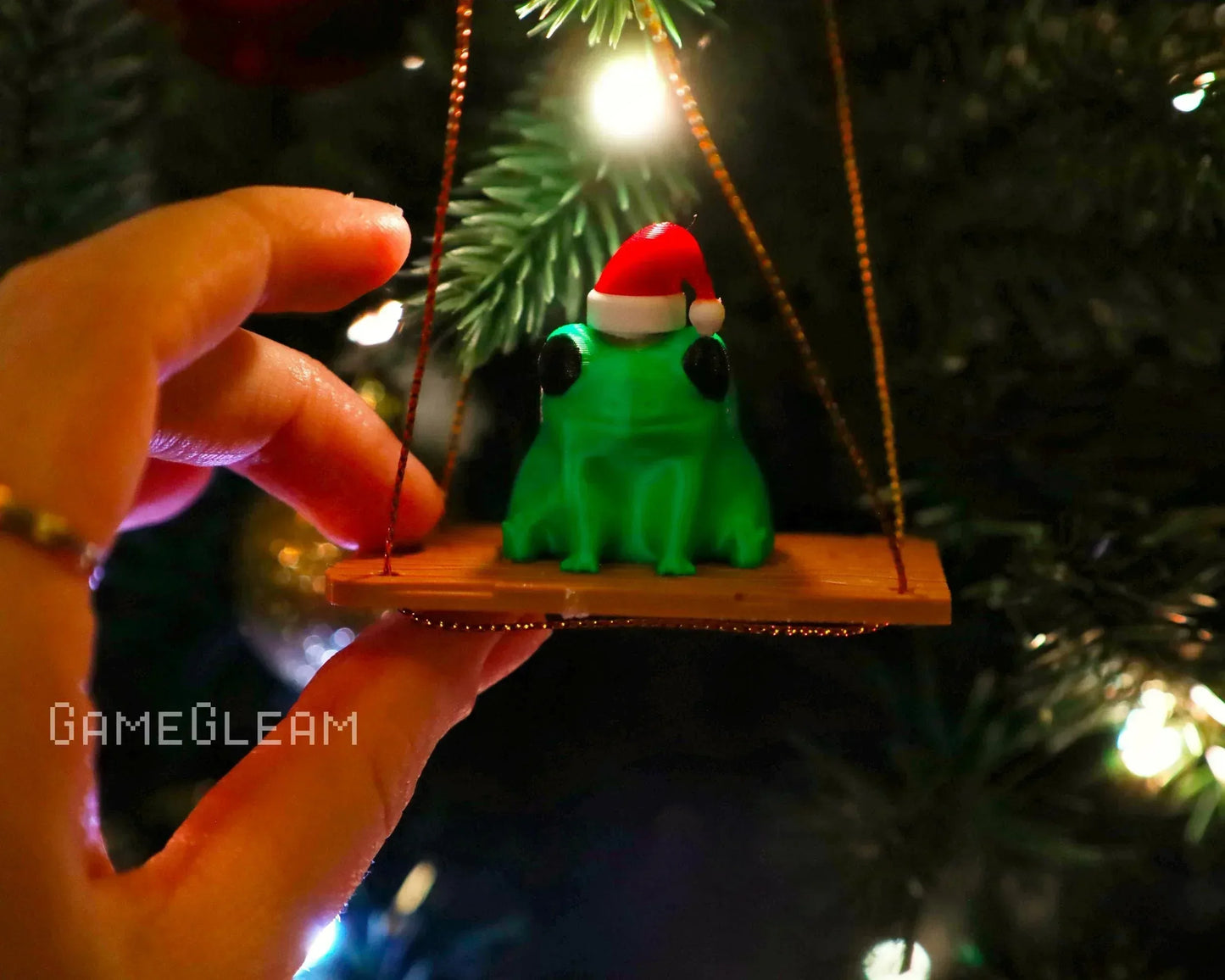 Green frog ornament with Santa hat on a swing, hanging on a Christmas tree