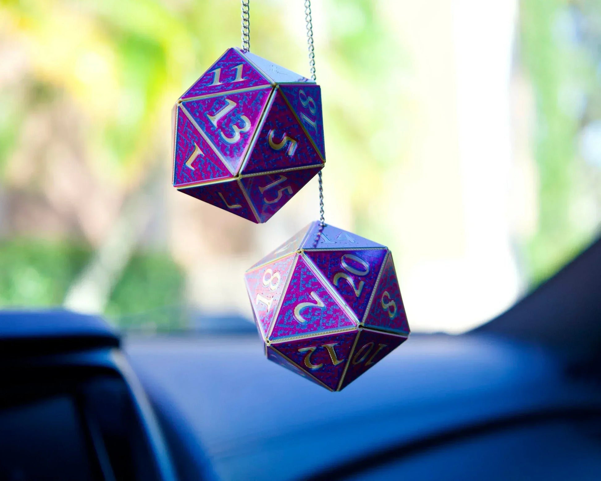 Holographic purple D20 dice car charms hanging from rearview mirror, blurred car interior