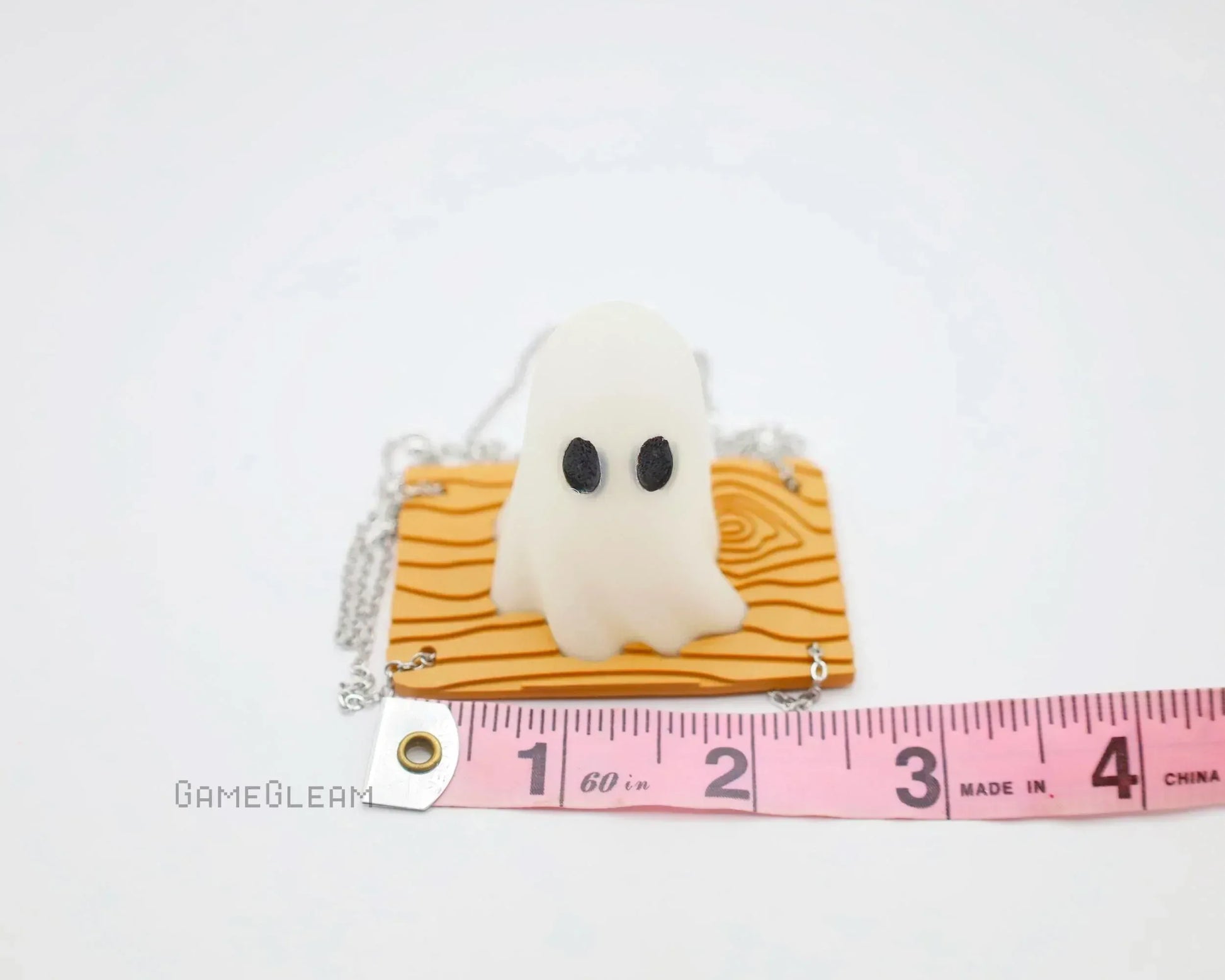 Handmade ghost charm with black eyes on textured orange base, next to a pink measuring tape
