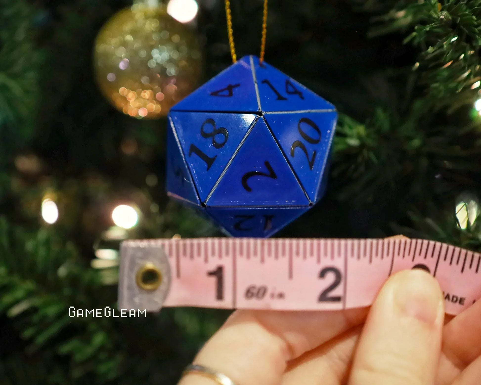 Blue 20-sided dice ornament measured with tape, hanging on a Christmas tree