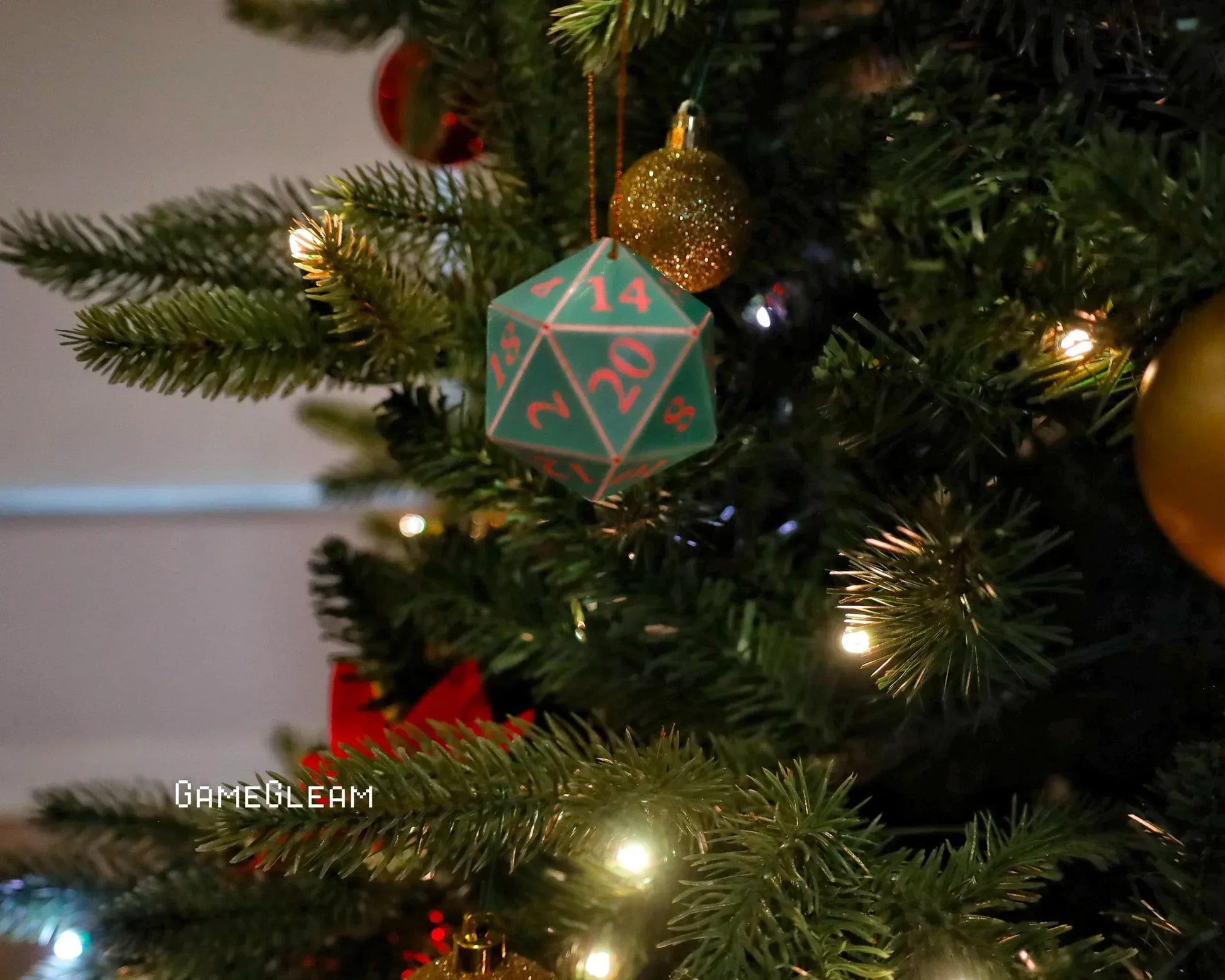 Green twenty-sided dice ornament hanging on a lit Christmas tree with gold baubles