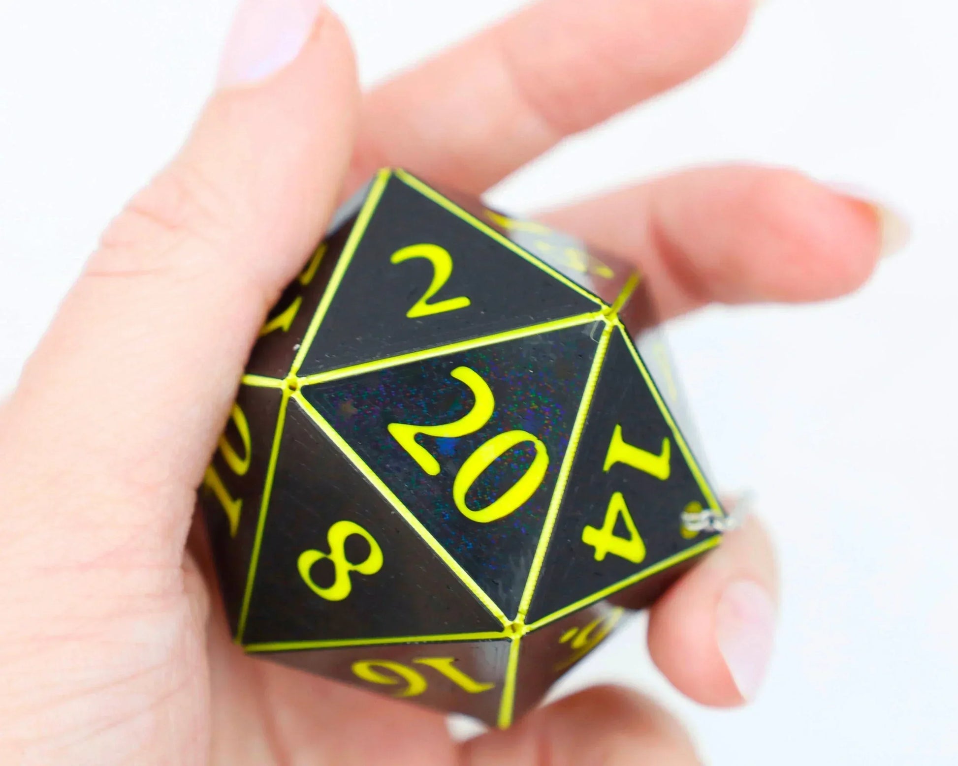 Hand holding a black holographic 20-sided dice with bright yellow numbers