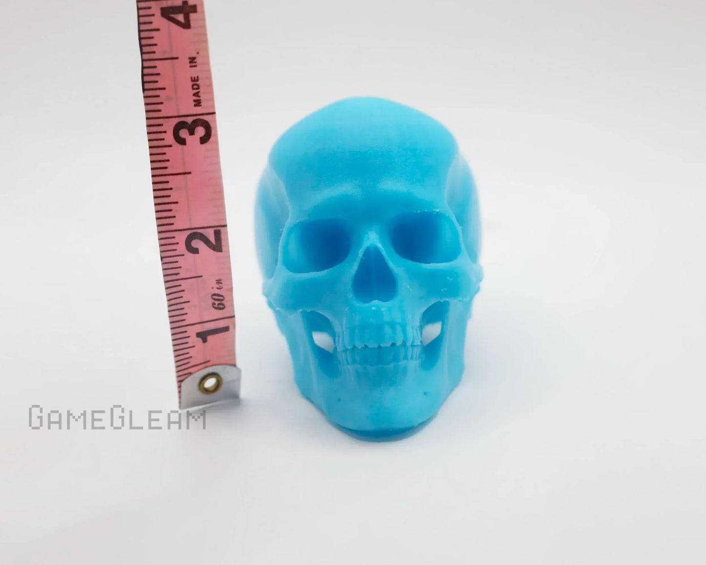 Blue resin skull figurine next to measuring tape on white background, gamer decor accessory