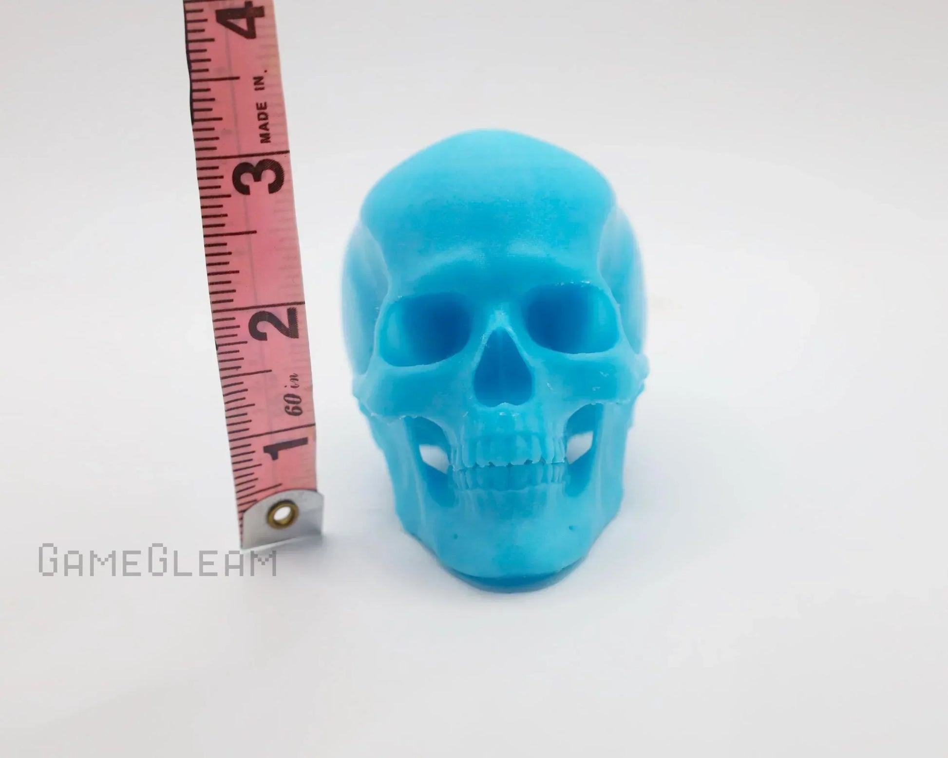 Blue resin skull figurine next to measuring tape on white background, gamer decor accessory