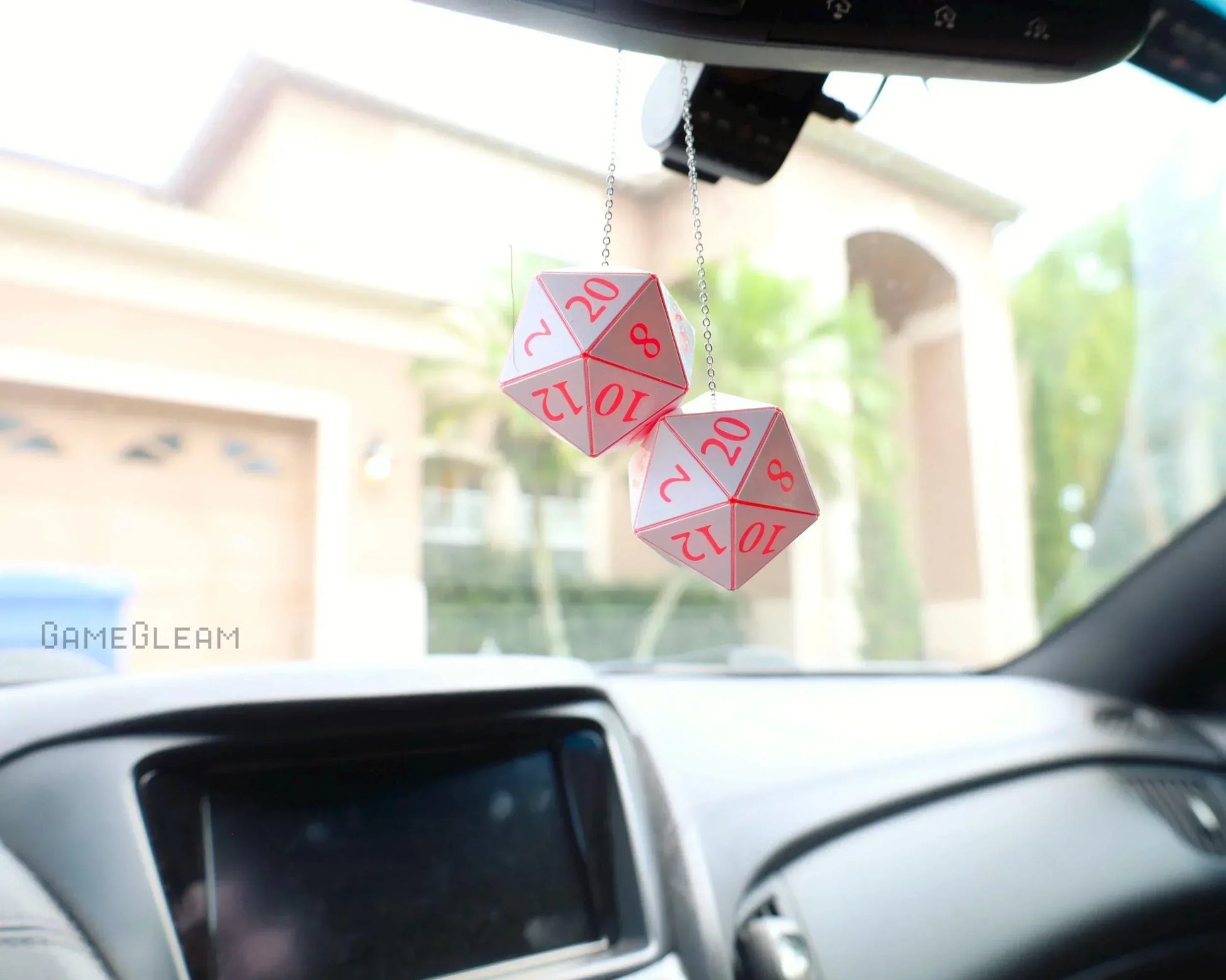 Pink and white twenty-sided dice car charm hanging from rearview mirror inside a vehicle.