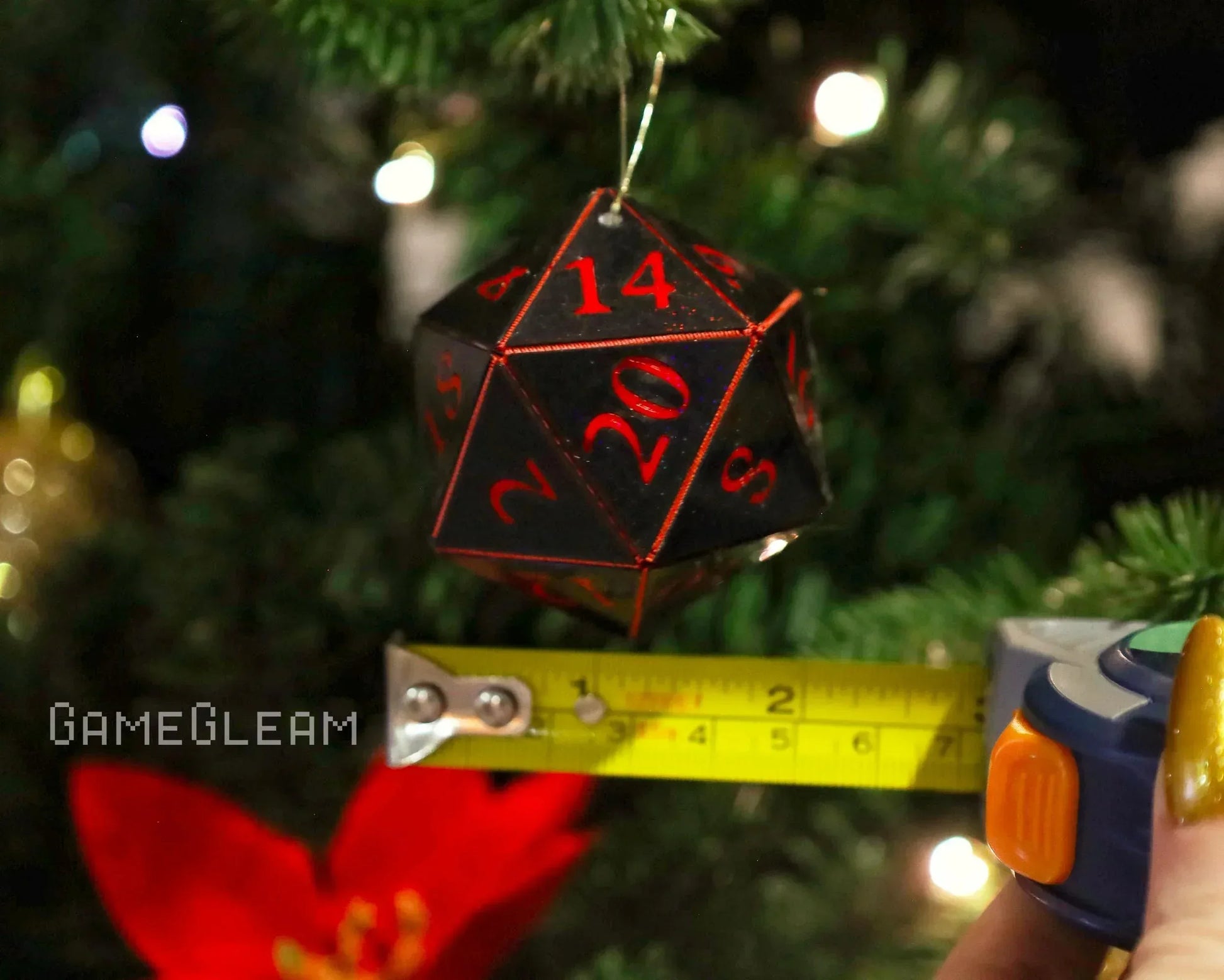 Black and red twenty-sided dice ornament hanging on a Christmas tree with measuring tape.