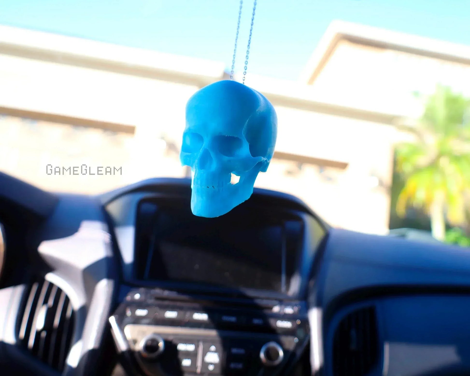 Blue skull car dice charm hanging from rearview mirror in a modern car interior
