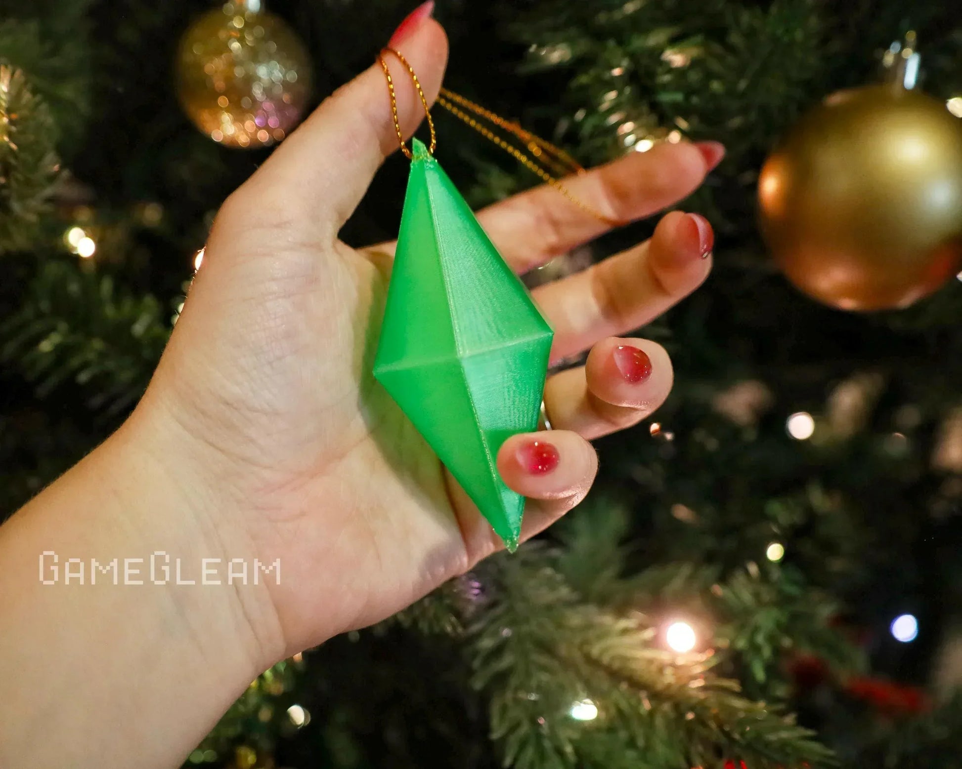 Hand holding a green geometric ornament in front of a decorated Christmas tree