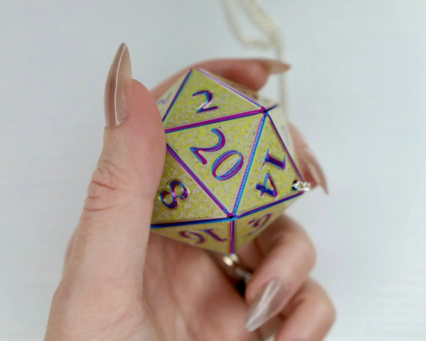 Hand holding large holographic yellow 20-sided dice car charm with purple numbers