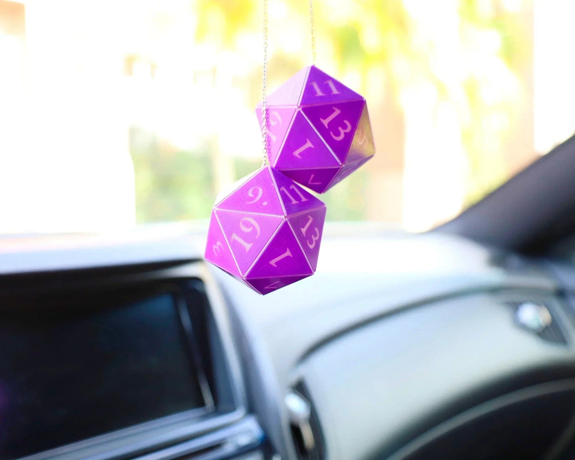 Purple twenty-sided dice car charm hanging from rearview mirror inside a car