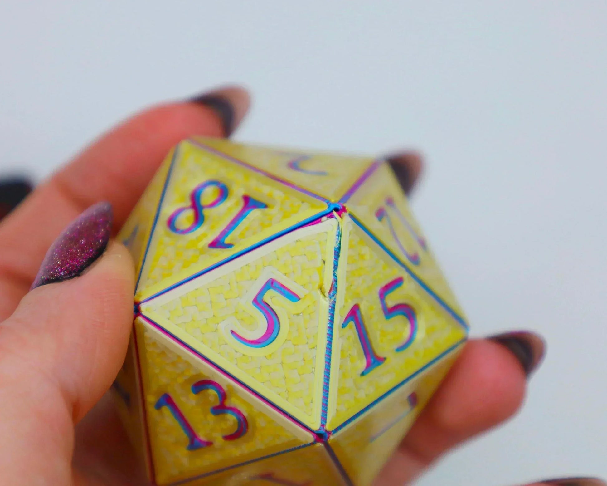 Hand holding a yellow holographic 20-sided jumbo dice with rainbow numbers, gaming accessory