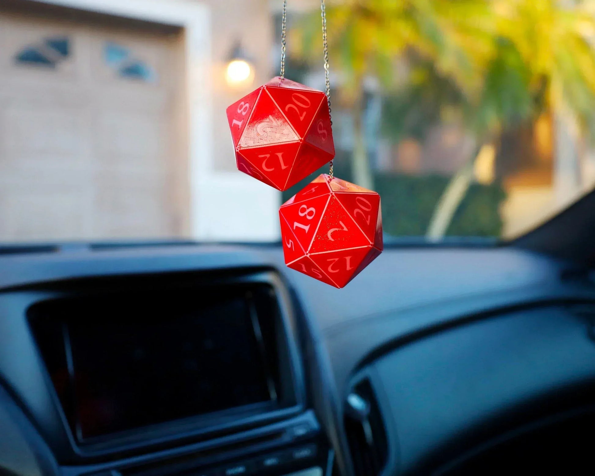 Red twenty-sided dice car charms hanging from rearview mirror in a car interior