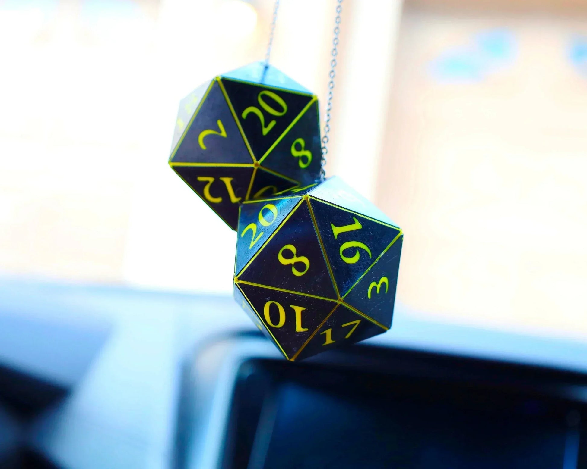 Hanging holographic twenty-sided dice car charm with yellow numbers, close-up in vehicle.