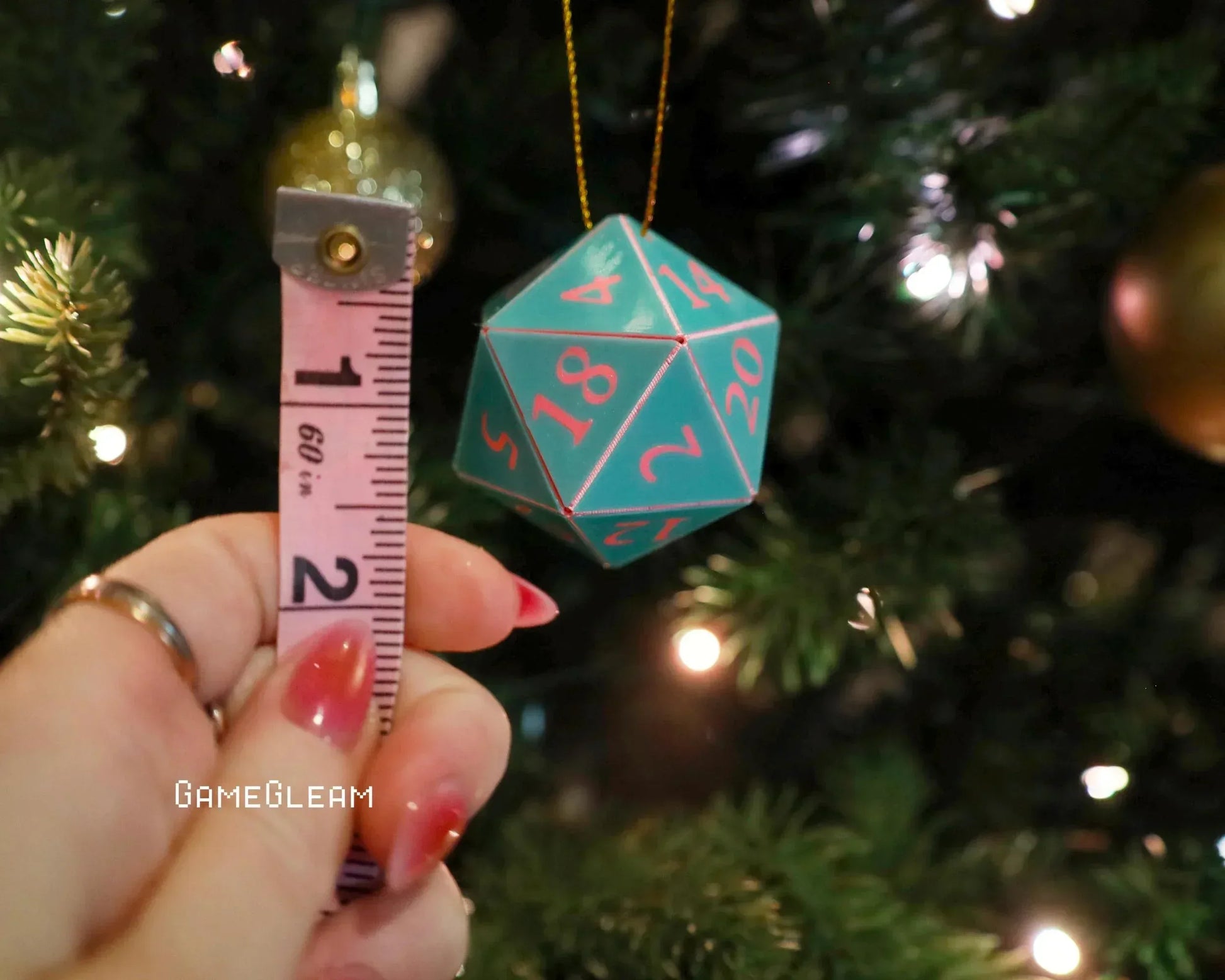 Hand holding tape measure next to teal twenty-sided dice ornament on Christmas tree
