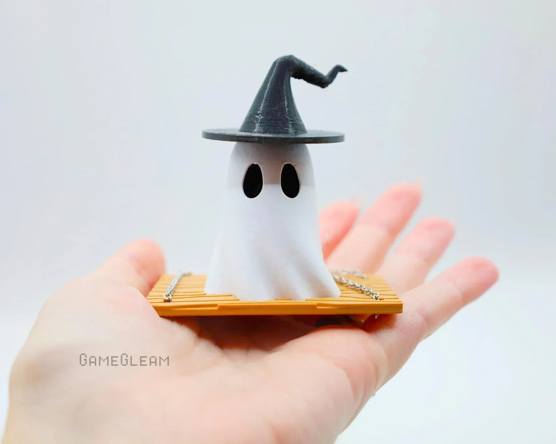 Hand holding a cute ghost figurine with witch hat on a wooden base, handmade gamer gift