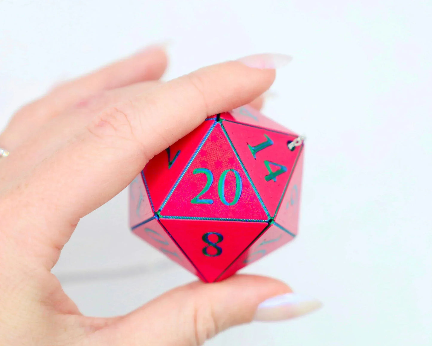 Hand holding a large holographic red 20-sided dice charm with teal numbers