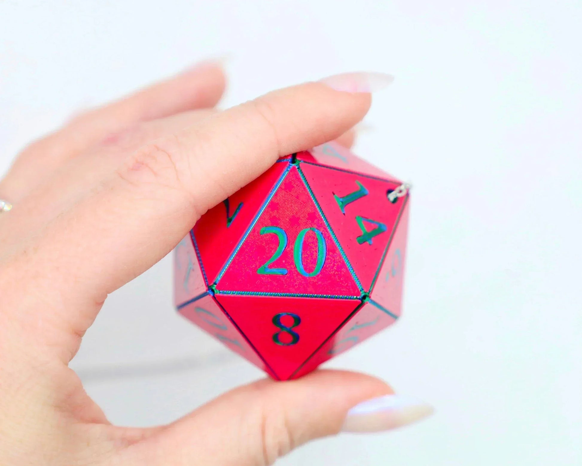 Hand holding a large holographic red 20-sided dice charm with teal numbers