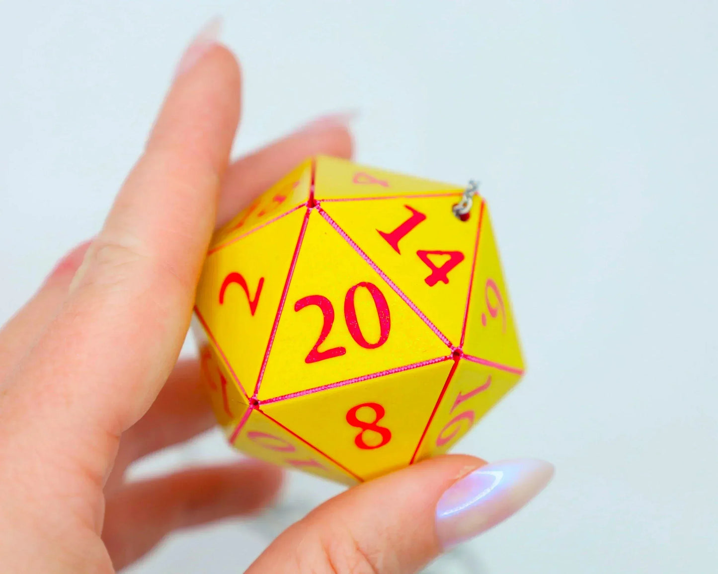 Hand holding a yellow twenty-sided dice charm with red numbers, used as a car accessory