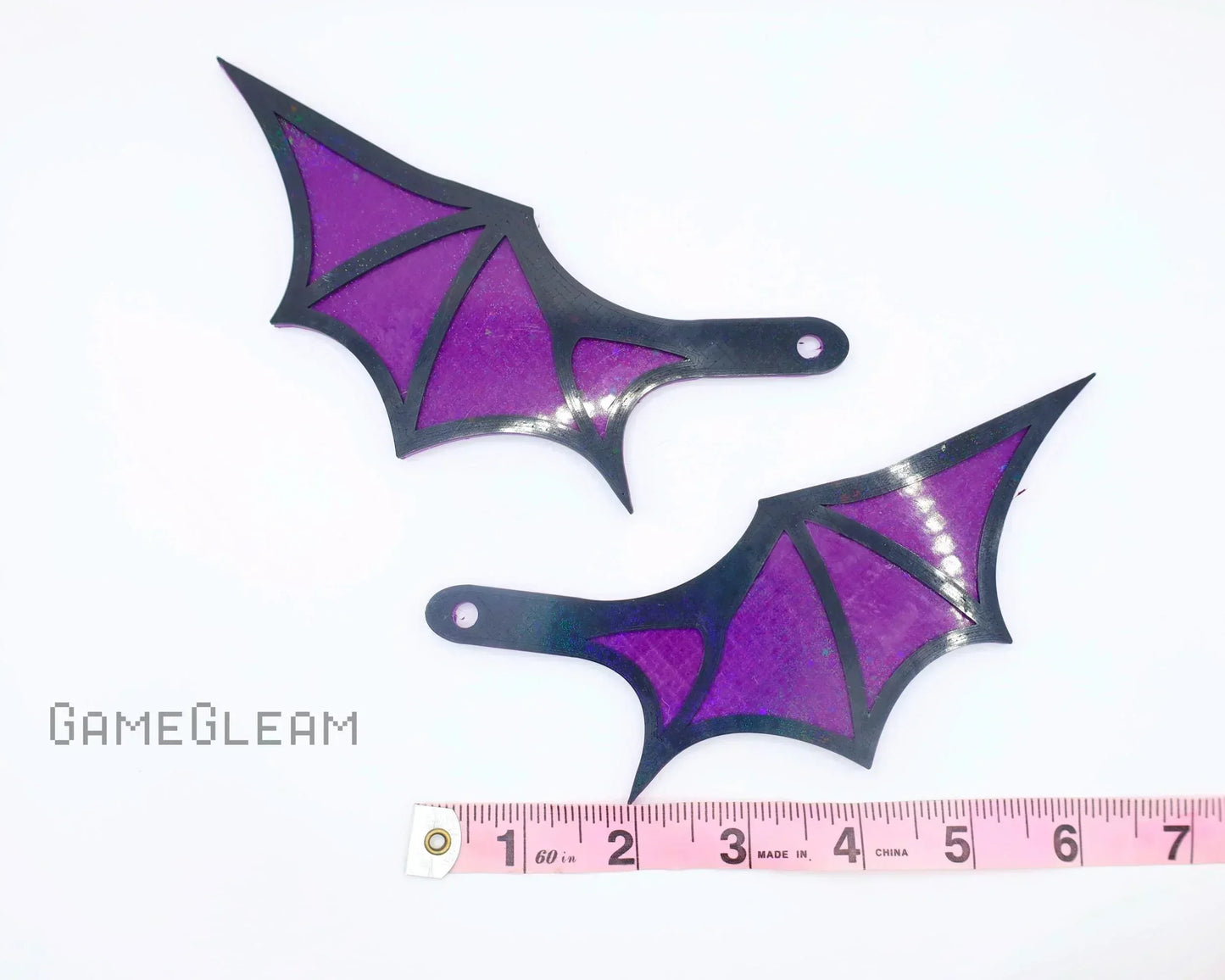 Pair of purple and black acrylic bat wing charms with measurement tape for scale