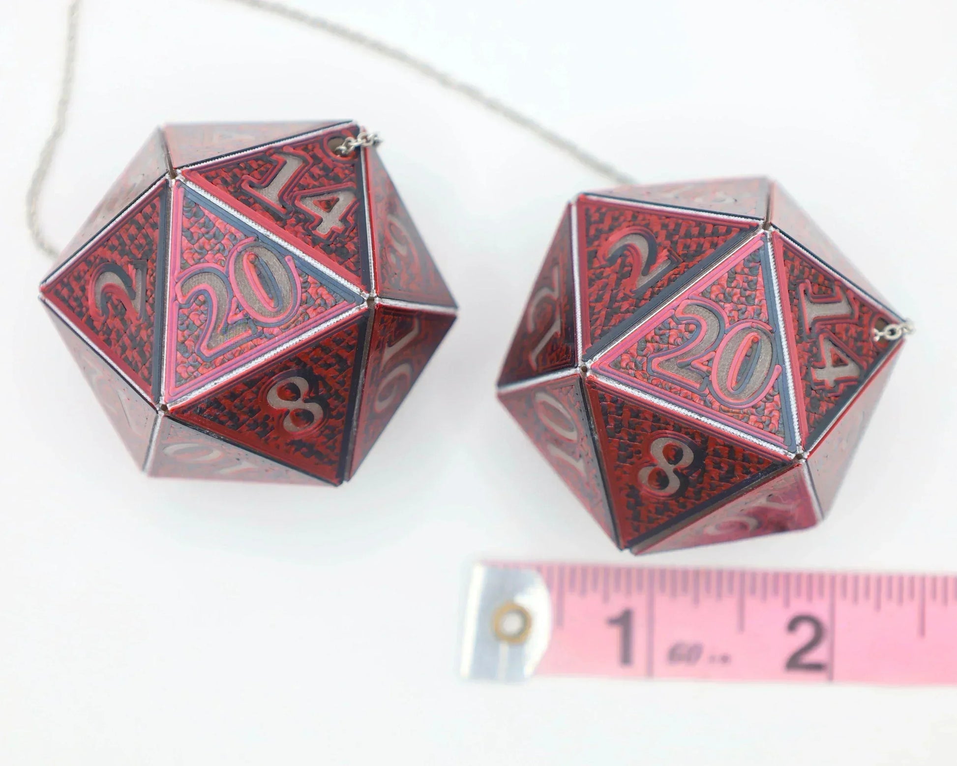 Pair of large red 20-sided polyhedral dice charms with chain, shown with measuring tape